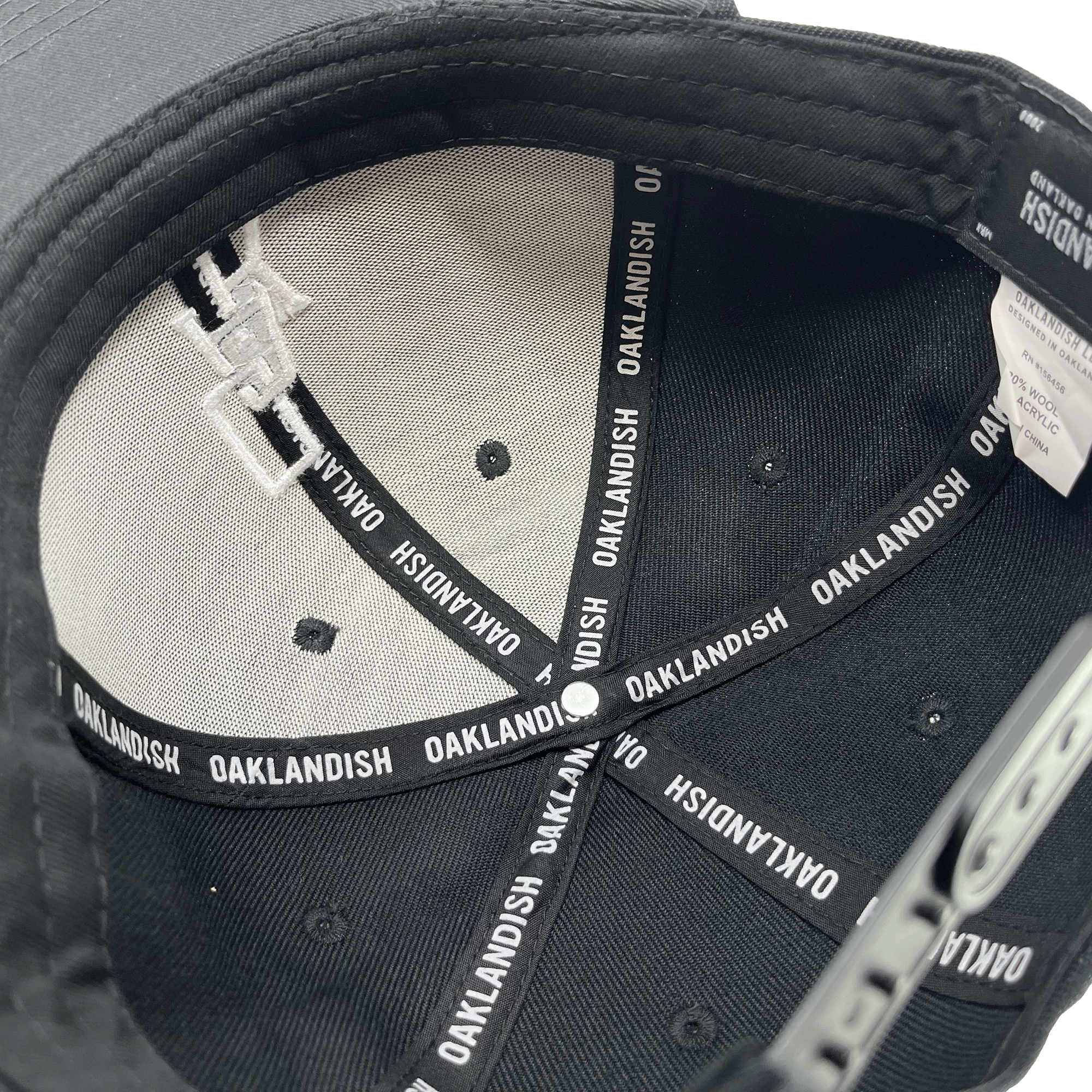 Inside crown view of a black cap with black striping with Oaklandish wordmark on repeat.