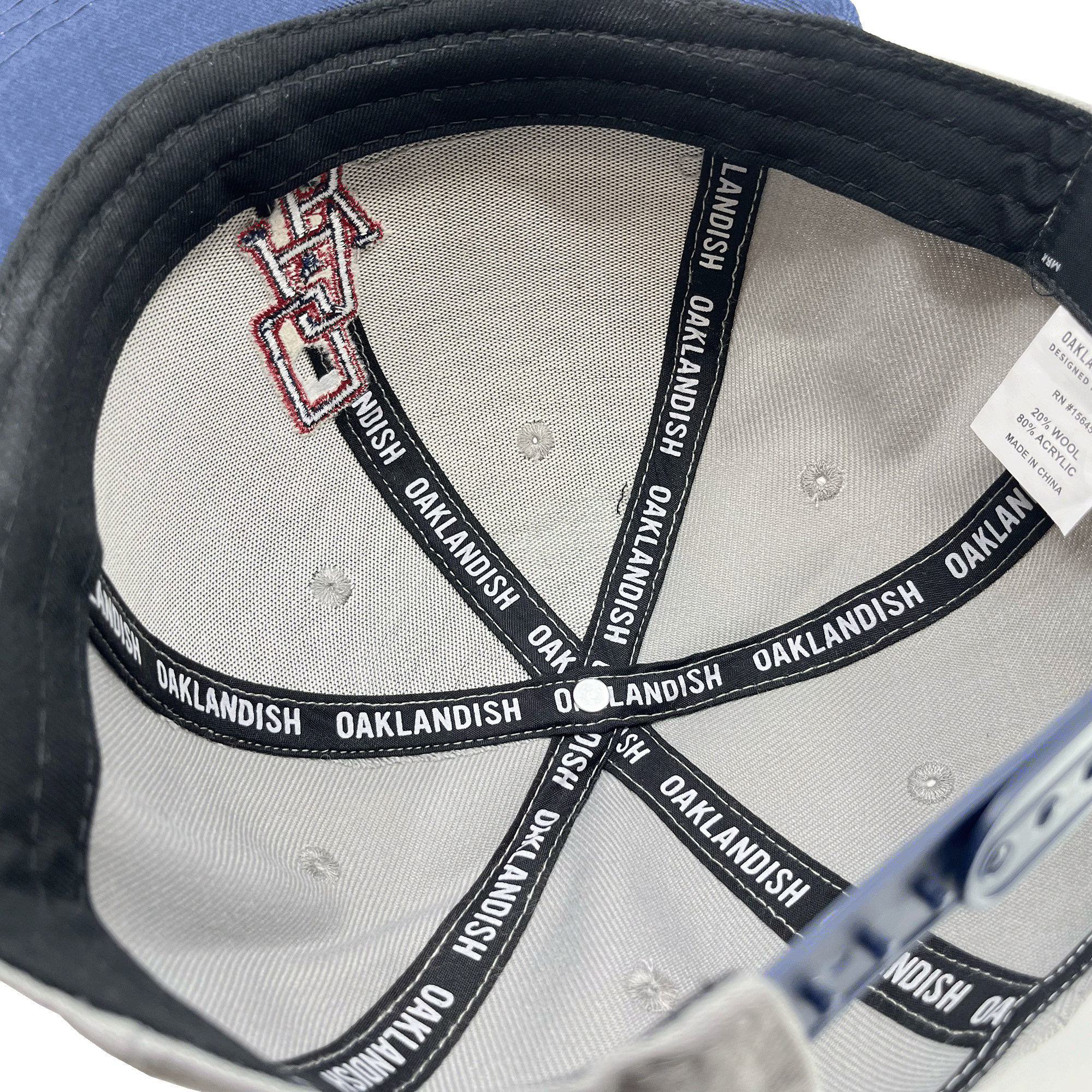 Inside crown view of a grey cap with black striping with Oaklandish wordmark on repeat.