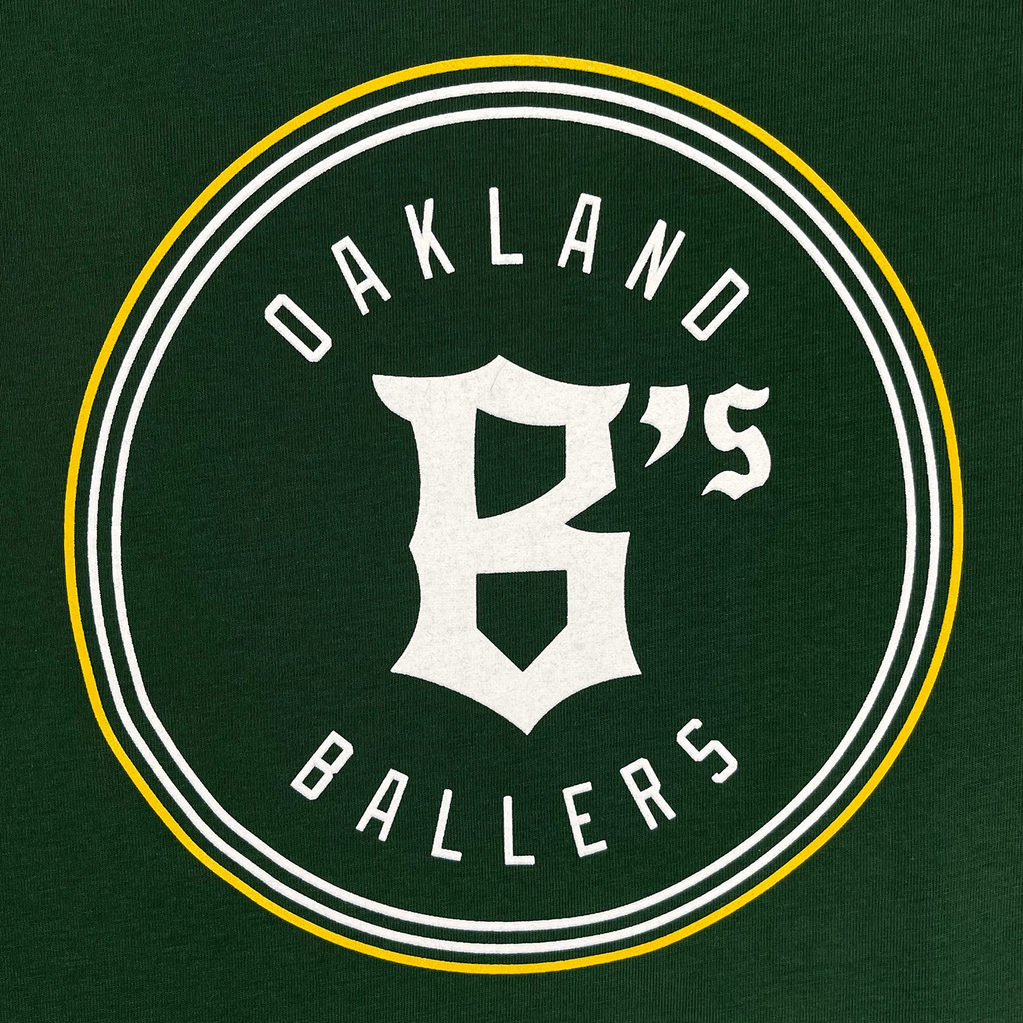 Detail photo of Oakland Ballers logo. White and Yellow circle with Oakland Ballers text on inside with B's in middle.