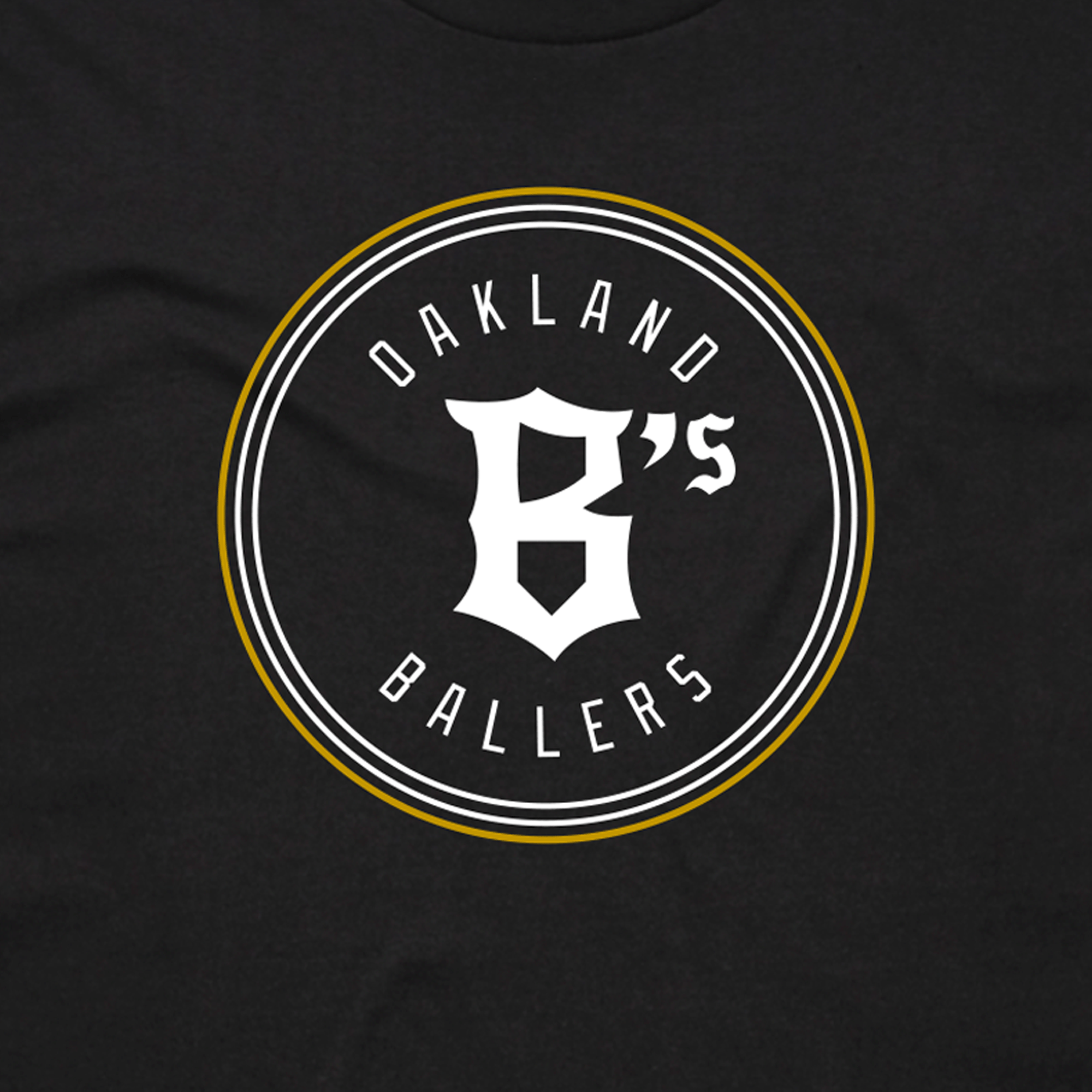 Close-up of the classic white and gold Oakland B's Ballers logo on the chest of a black t-shirt.
