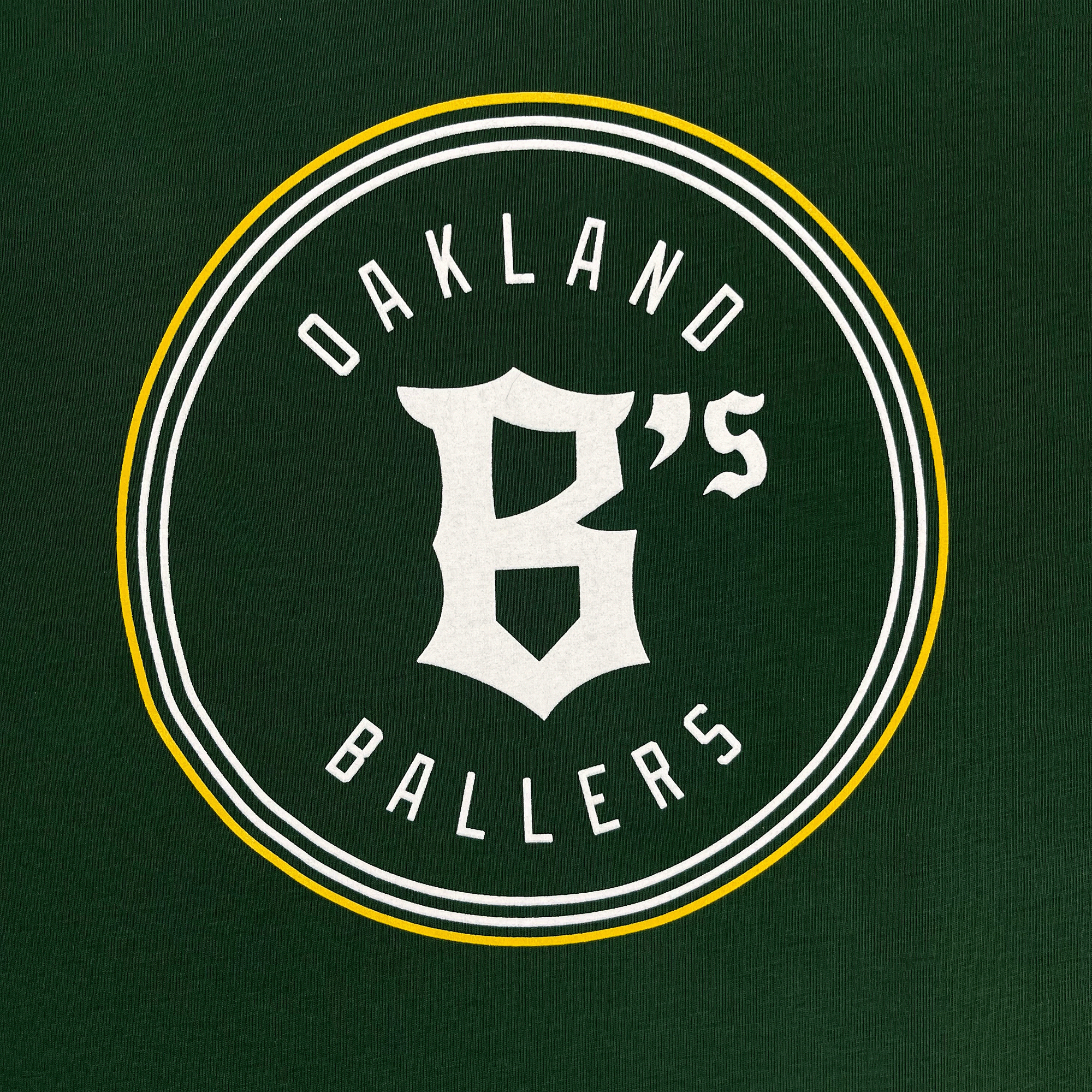 Close-up of Oakland B’s logo on the front chest of a green women’s t-shirt.