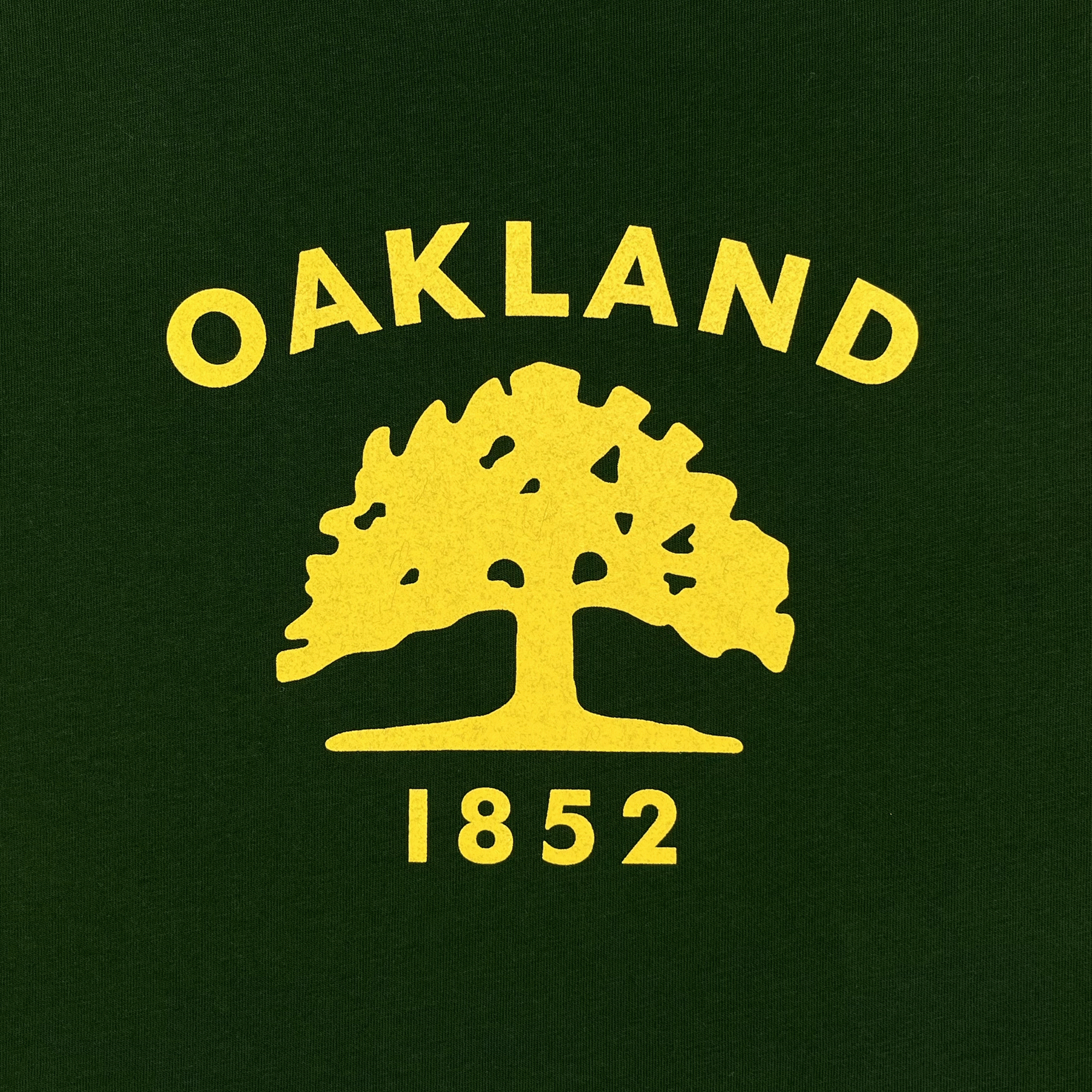 Detailed view of forest green t-shirt with yellow Oakland 1852 Flag graphic.