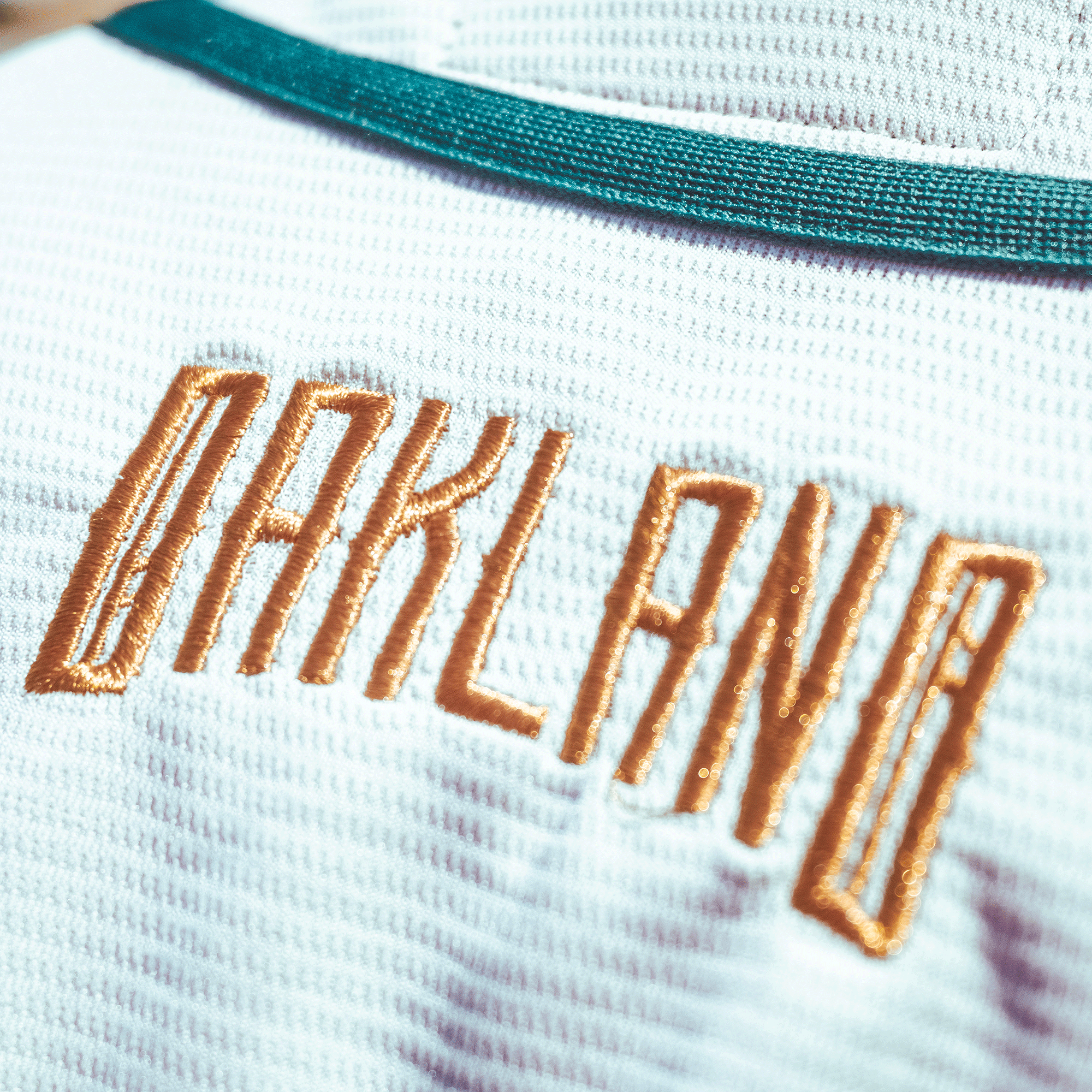Close-up of the Oakland Ballers Button Up Jersey by Oakland Ballers, featuring textured white fabric, teal trim, and "OAKLAND" in large gold vertical embroidery—highlighting premium stitching and pro baseball team pride.