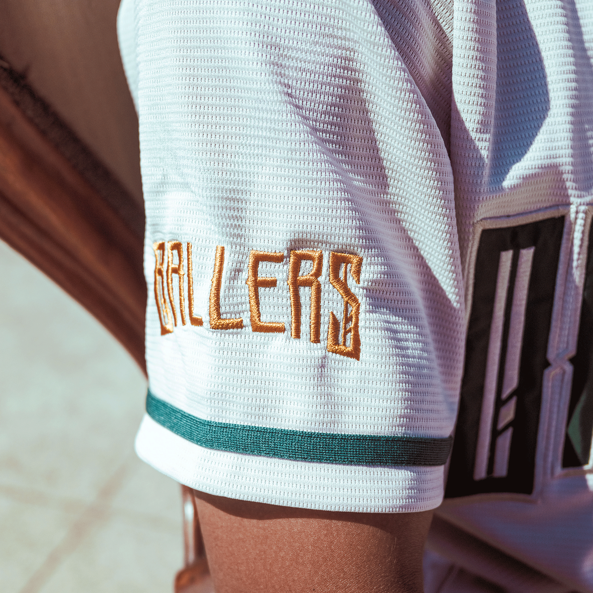 A close-up of a person’s upper arm wearing the Oakland Ballers Button Up Jersey, branded with green-striped sleeves and "BALLERS" in gold from the Oakland Ballers, a Pioneer League baseball team. The background is out of focus.