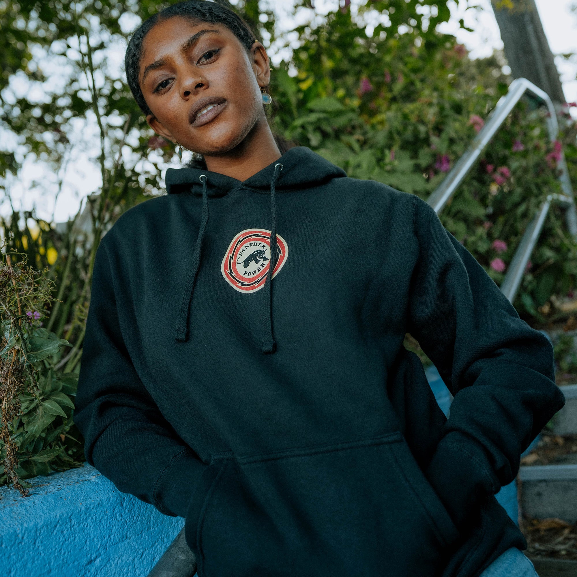 Front angle of female model wearing Educate to Liberate black hoodie with Panther power emblem at front center.