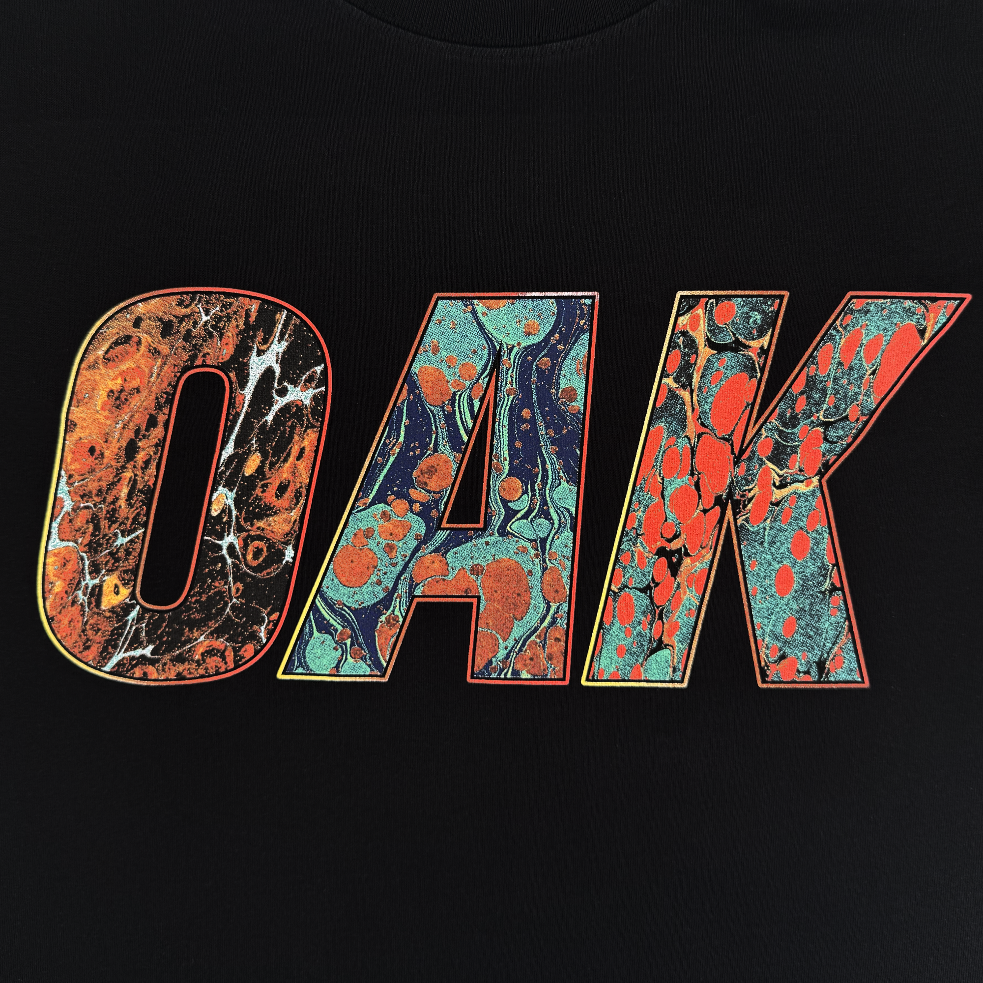 The Oil and Water Tee by Oaklandish features the word “OAK” in bold letters with vibrant marbled patterns on a black background, making it a striking classic-fit men’s t-shirt crafted from heavy-weight cotton.