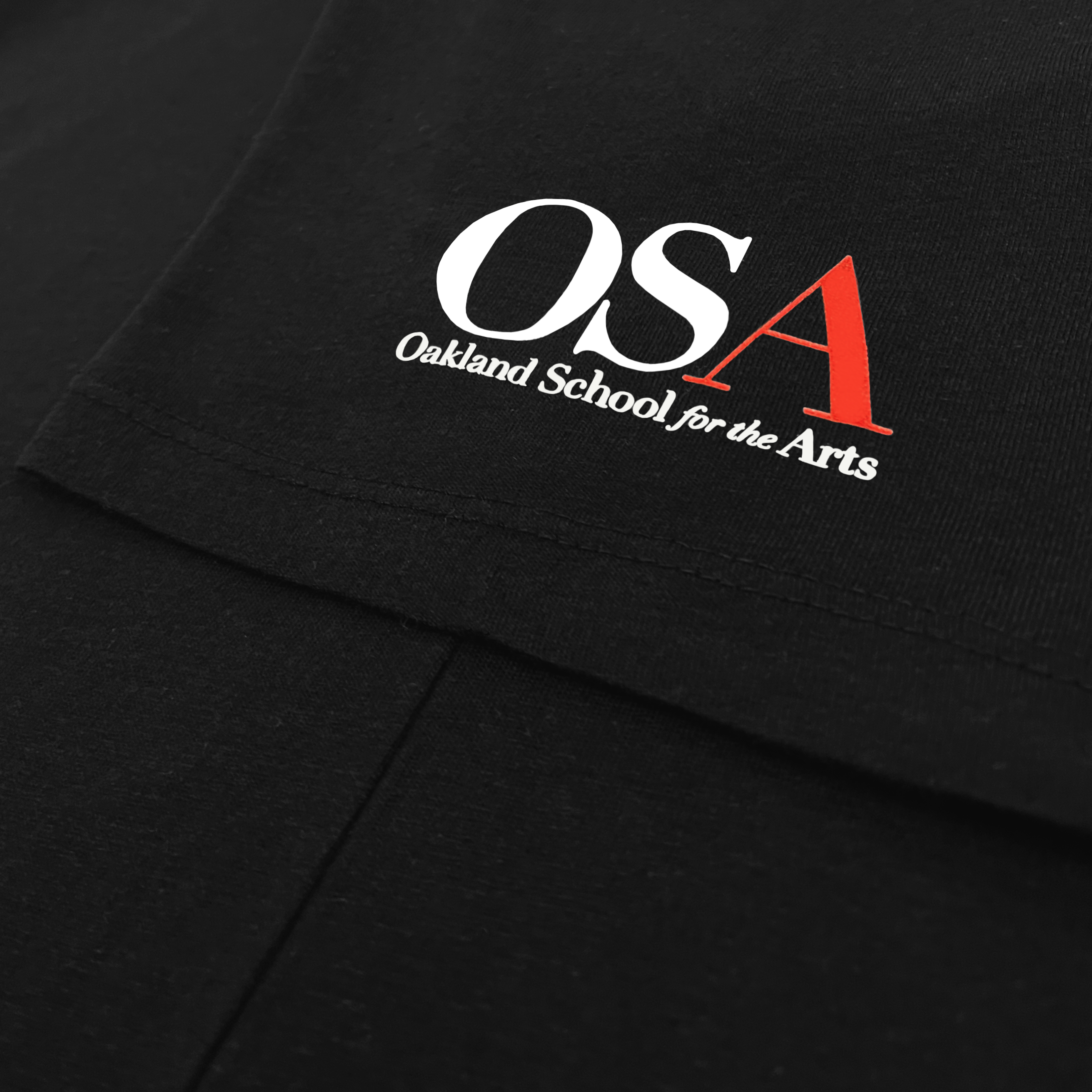Close-up of the sleeve of a black t-shirt with OSA, Oakland School for the Arts logo and wordmark.