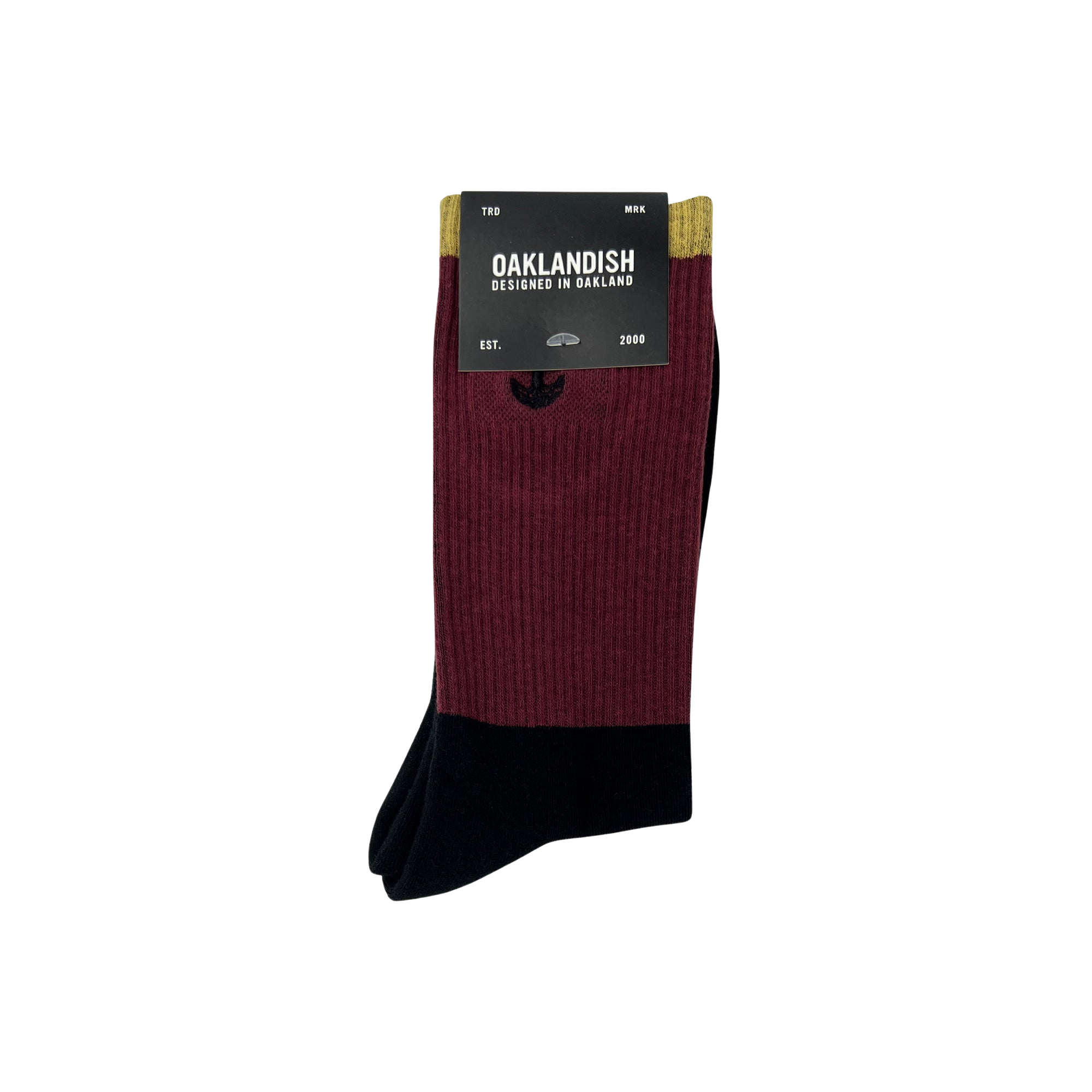A pair of Colorblock Socks by Oaklandish features a maroon upper part and a black lower part. The packaging label reads "OAKLANDISH, Designed in Oakland, Est. 2000," and includes an embroidered Oaklandish logo along with an emblem of oak trees. Size is indicated as "TBD" and material as "MRR.