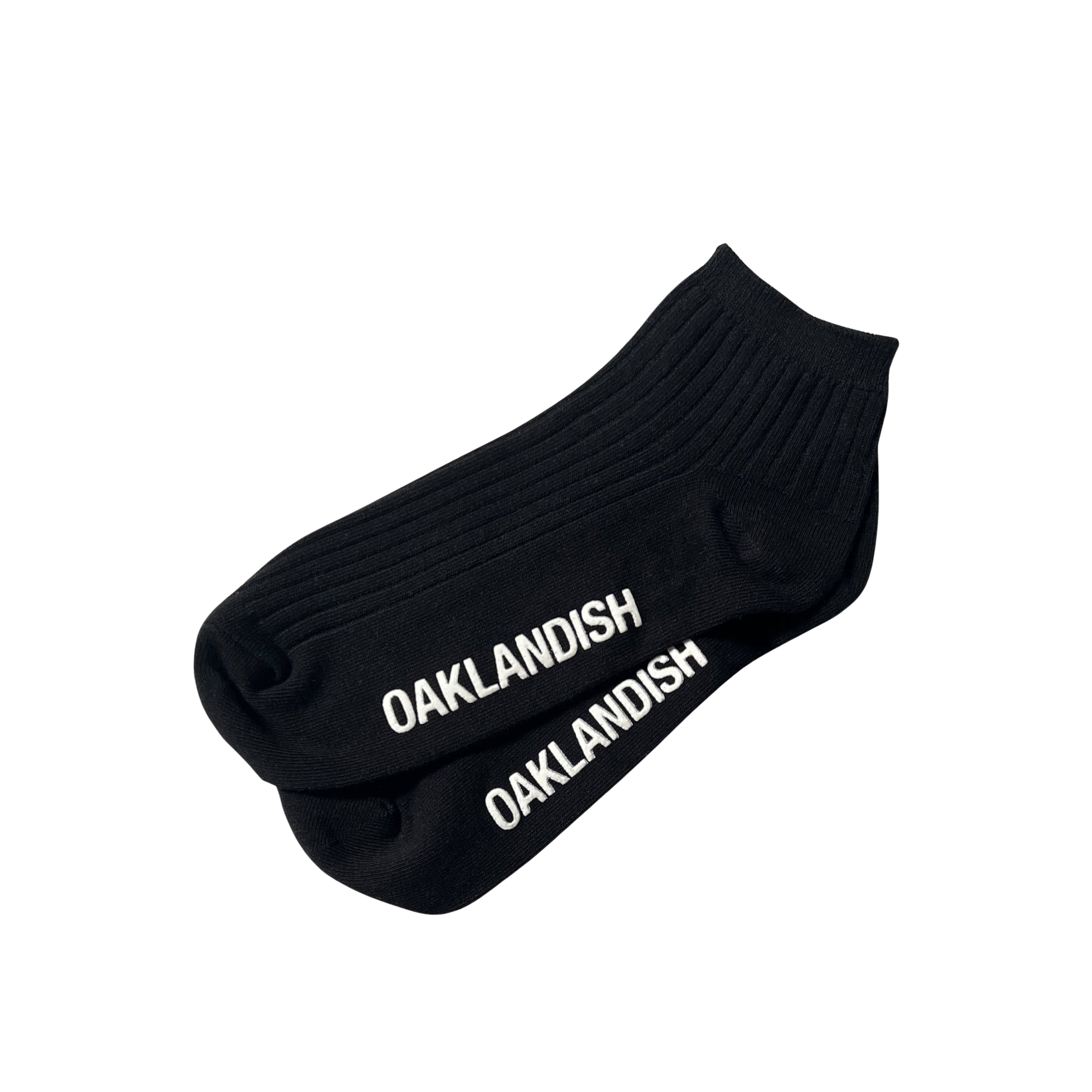 A pair of Grip Low Crew Socks from Oaklandish, featuring a black, ribbed design with "OAKLANDISH" printed in white capital letters along the top, are laid flat against a plain white background.