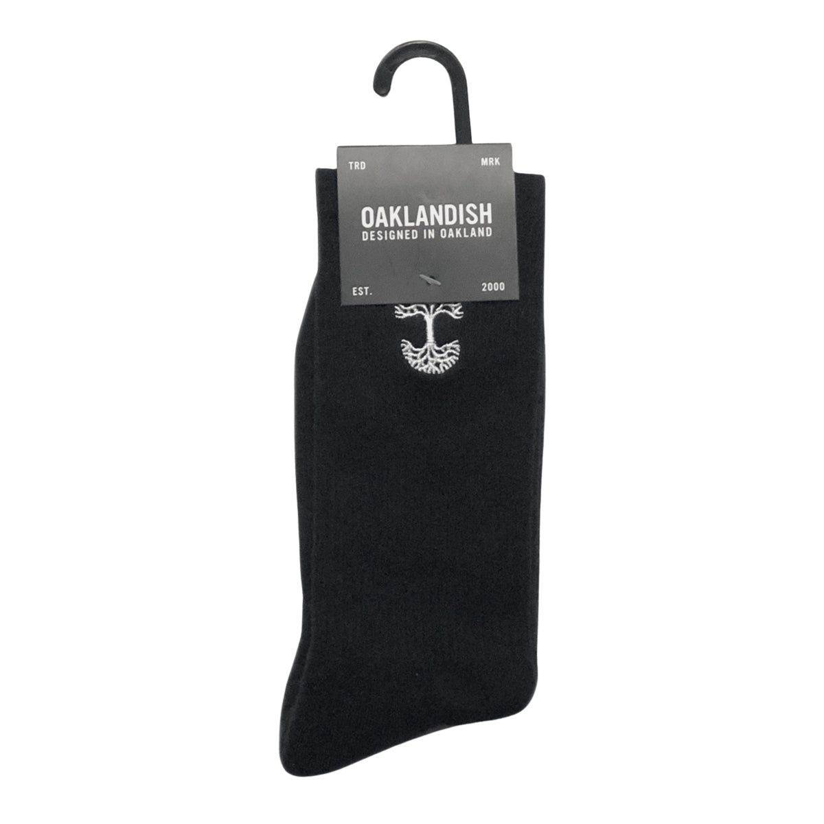 A single black Embroidered Logo Sock from Oaklandish is displayed on a hanger, with a label attached at the top. The label reads "OAKLANDISH DESIGNED IN OAKLAND" along with "TRD MRK" on either side. The year "EST. 2000" is also mentioned. An emblem resembling a tree appears on the adult-sized Oaklandish sock below the label.