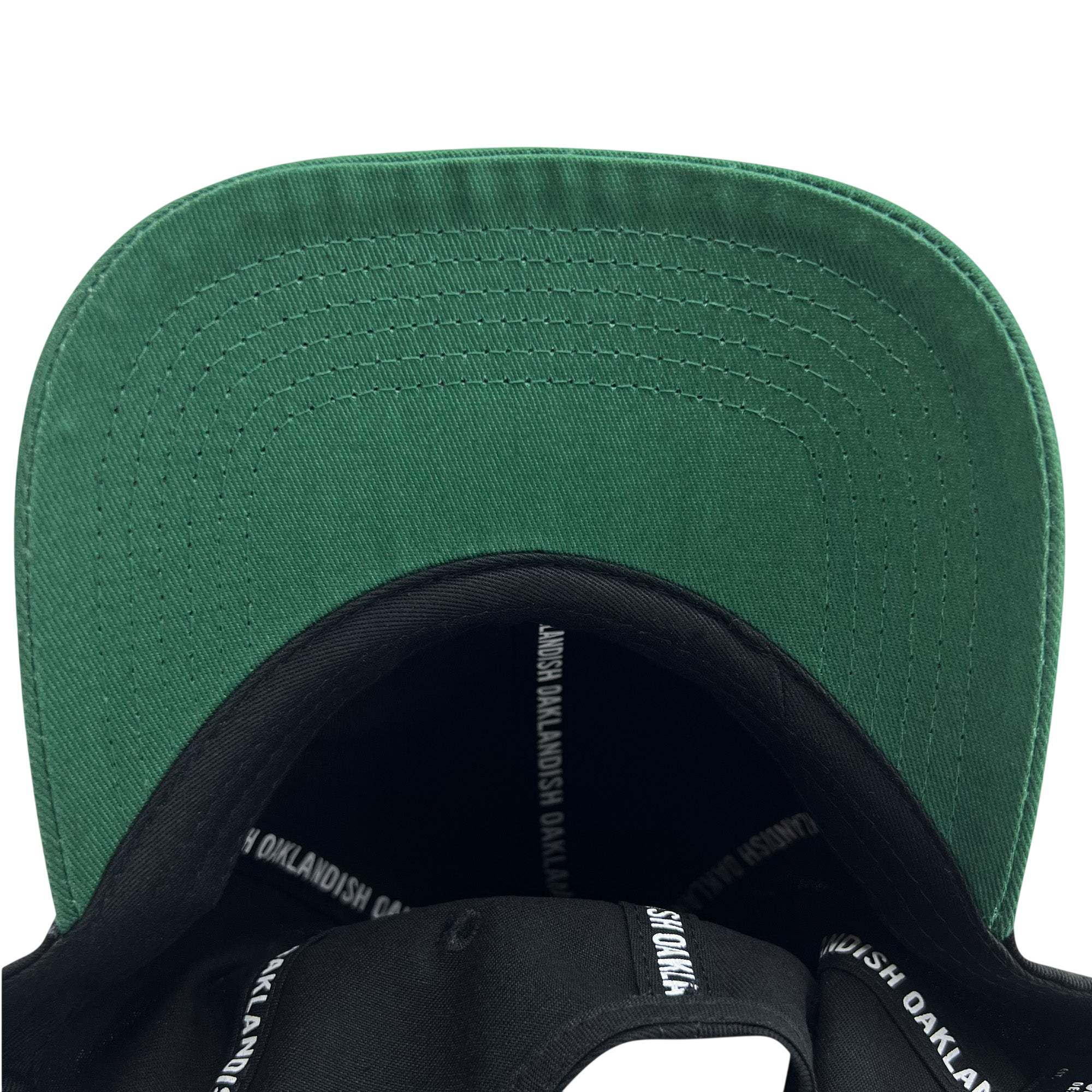 A close-up view of the underside of the Official Micro Logo Dad Hat's green brim. The inner band is black, adorned with "OAKLANDISH" repeatedly printed in white. From this bottom-up perspective, you can also notice an embroidered "O," adding a unique touch to the Oaklandish design.