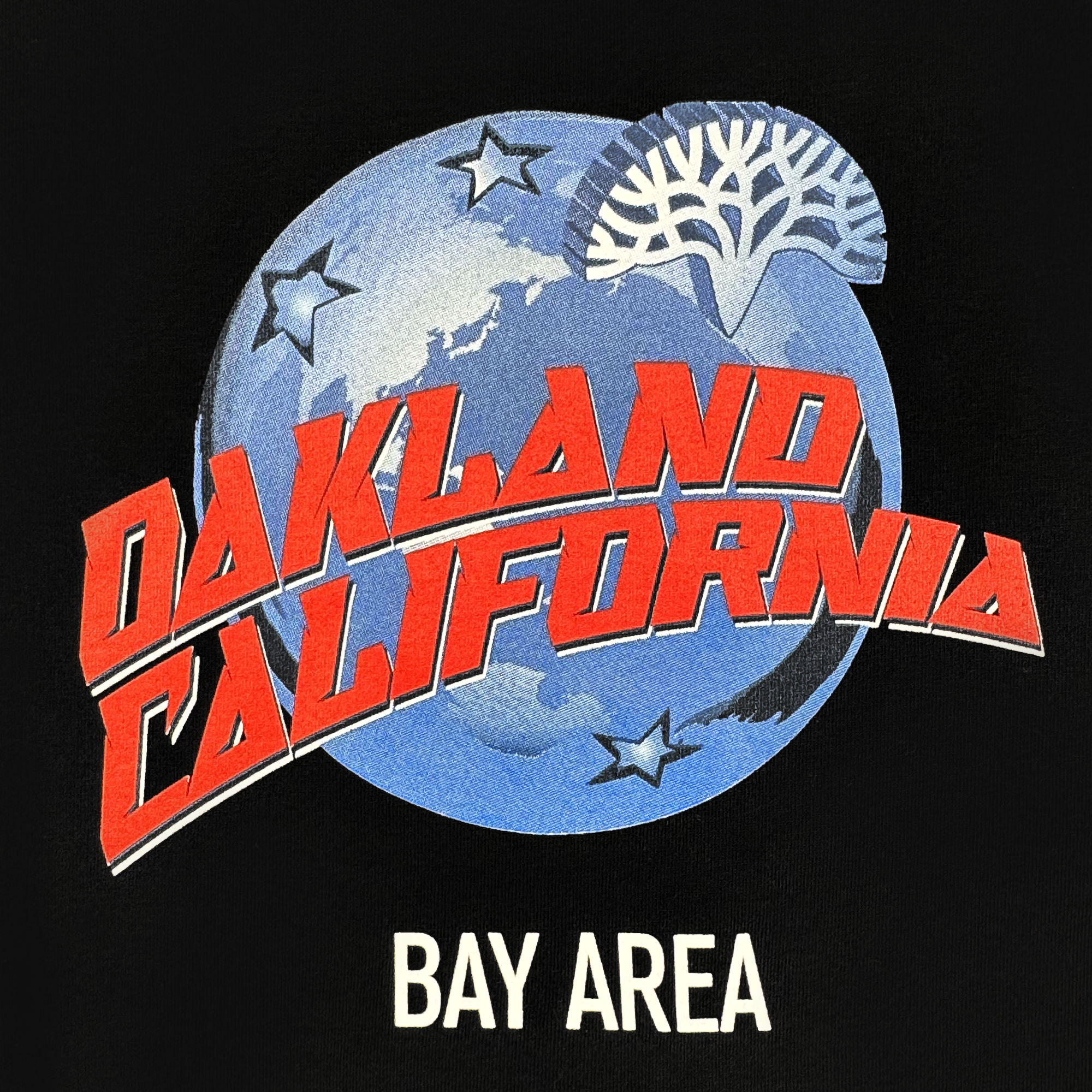 The Planet Oakland Tee by Oaklandish features a blue Earth with white stars and a stylized tree. Bold red “OAKLAND CALIFORNIA” spans the globe, with “BAY AREA” in white below, all on soft 100% cotton.