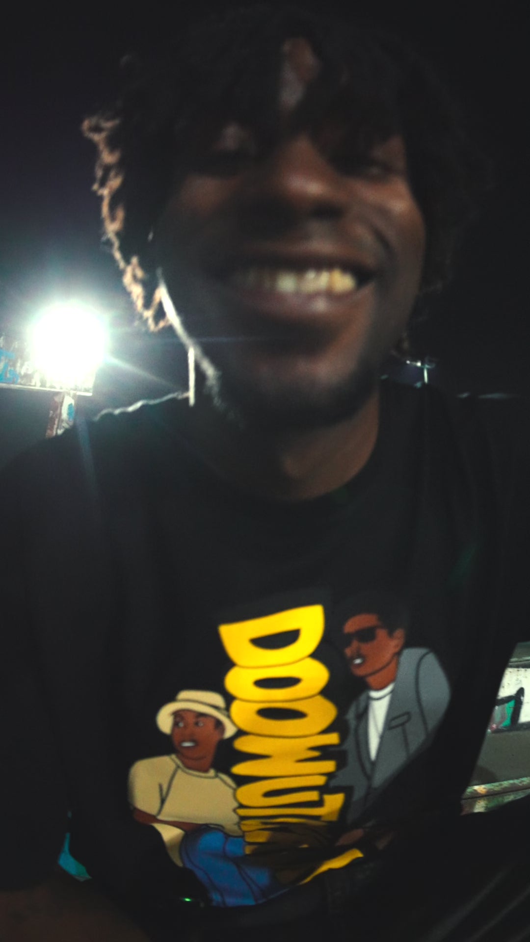 Model smiling and wearing a collab tee in the nighttime.