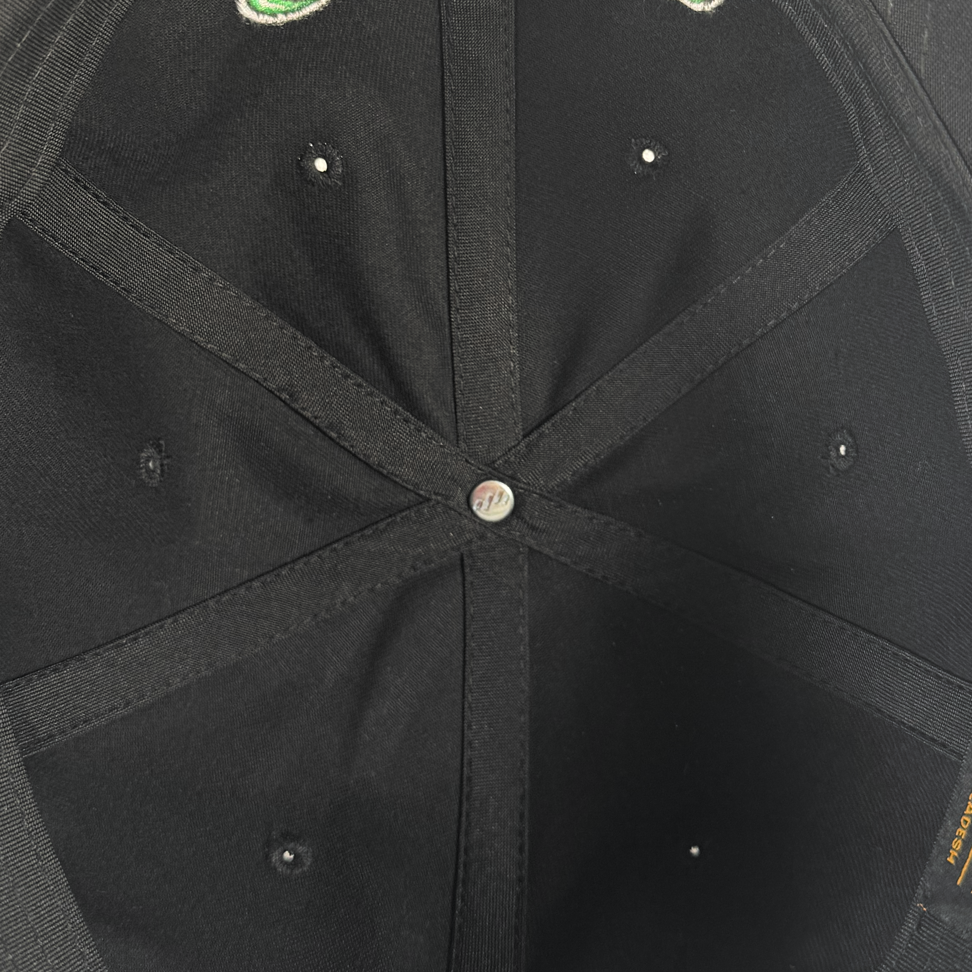 Close-up of the inside crown of the Oakland Roots SC X Break Free Hat by Oakland Roots SC, featuring stitched black panels radiating from a central silver button, metal ventilation eyelets, and an orange tag on the right edge.