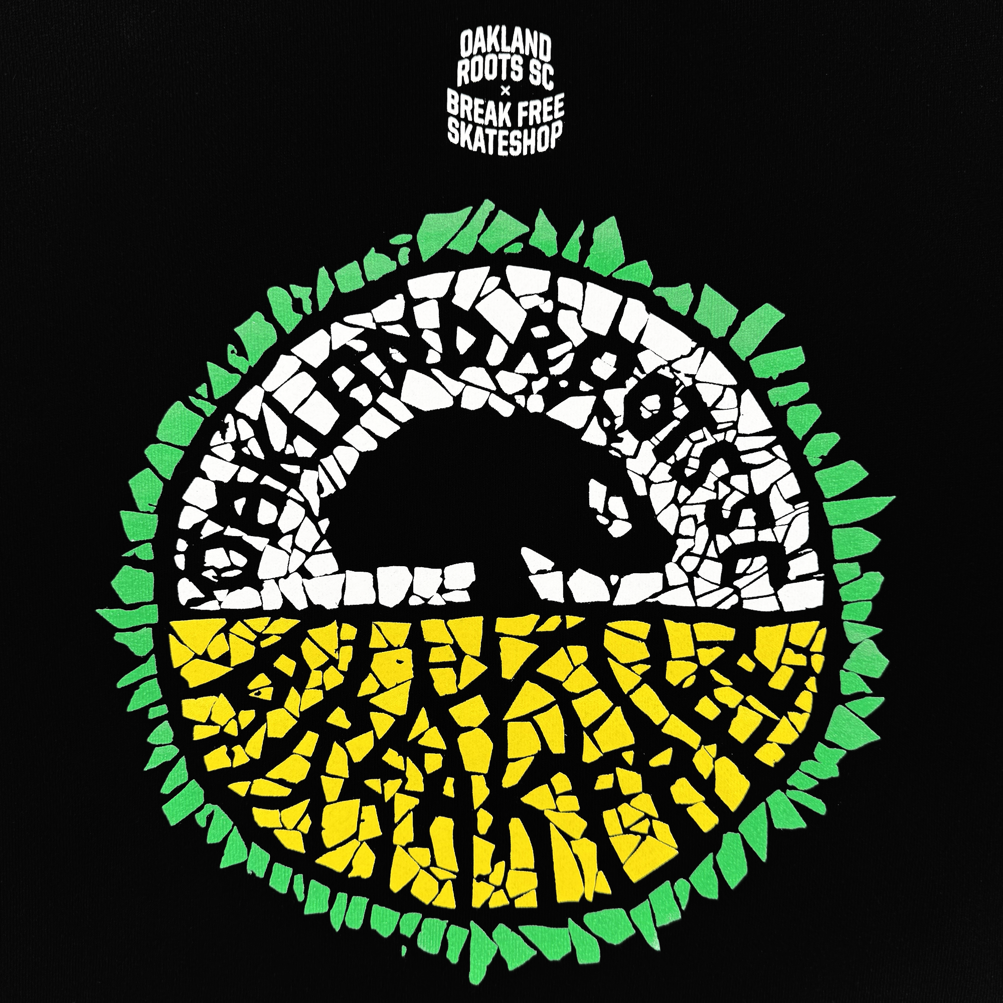 The Oakland Roots SC X Break Free Tee features a circular mosaic logo with “OAKLAND ROOTS” in white around a black bear silhouette. The top is white, the bottom yellow with green roots. "OAKLAND ROOTS SC x BREAK FREE SKATESHOP" appears above in white on black.