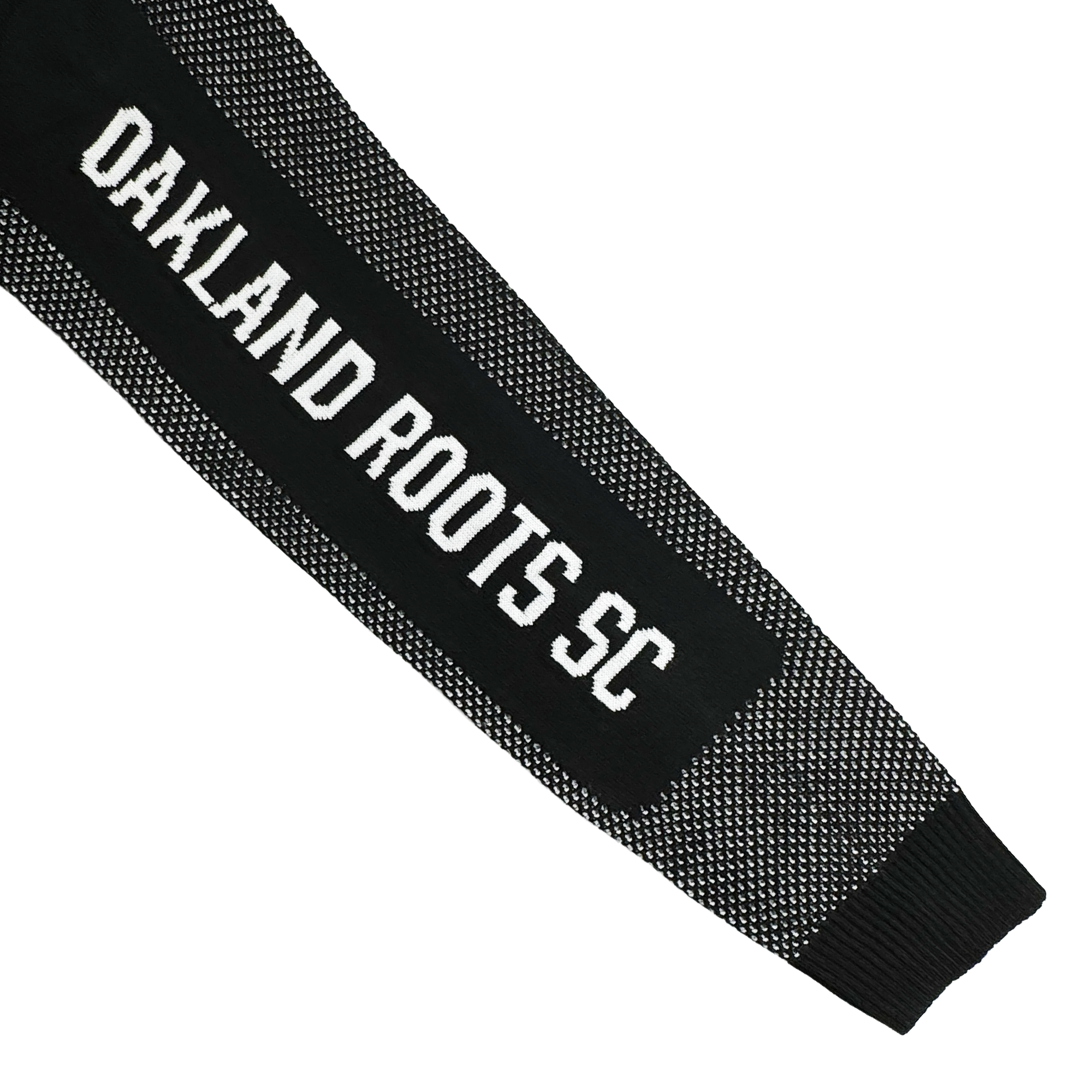 The Oakland Roots SC Clubhouse Sweater by Oakland Roots SC features black knit fabric with a white grid pattern on the cuffs and edges. Bold white “OAKLAND ROOTS SC” text appears on the sleeve against a plain white background.