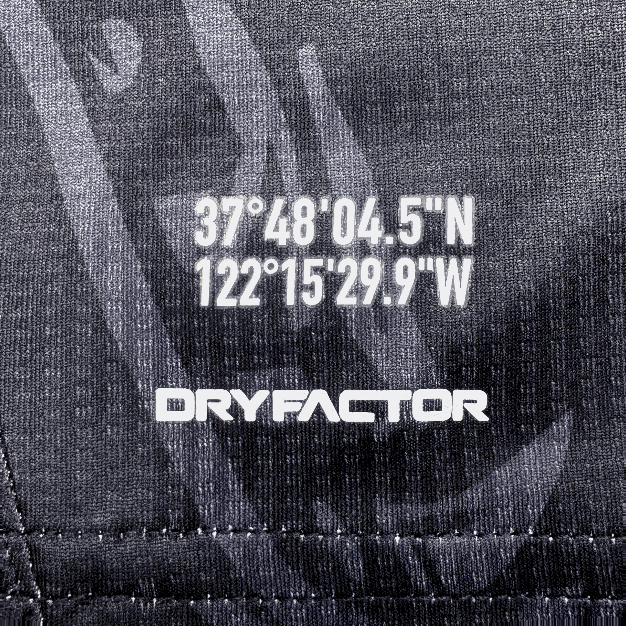 Close-up of dark, textured fabric from the Oakland Roots SC Custom Unisex Oak-ness Awakens Kit with white coordinates "37°48'04.5''N 122°15'29.9''W," "DRYFACTOR" below, and subtle stitching evoking Lake Merritt’s Oak-ness Monster.