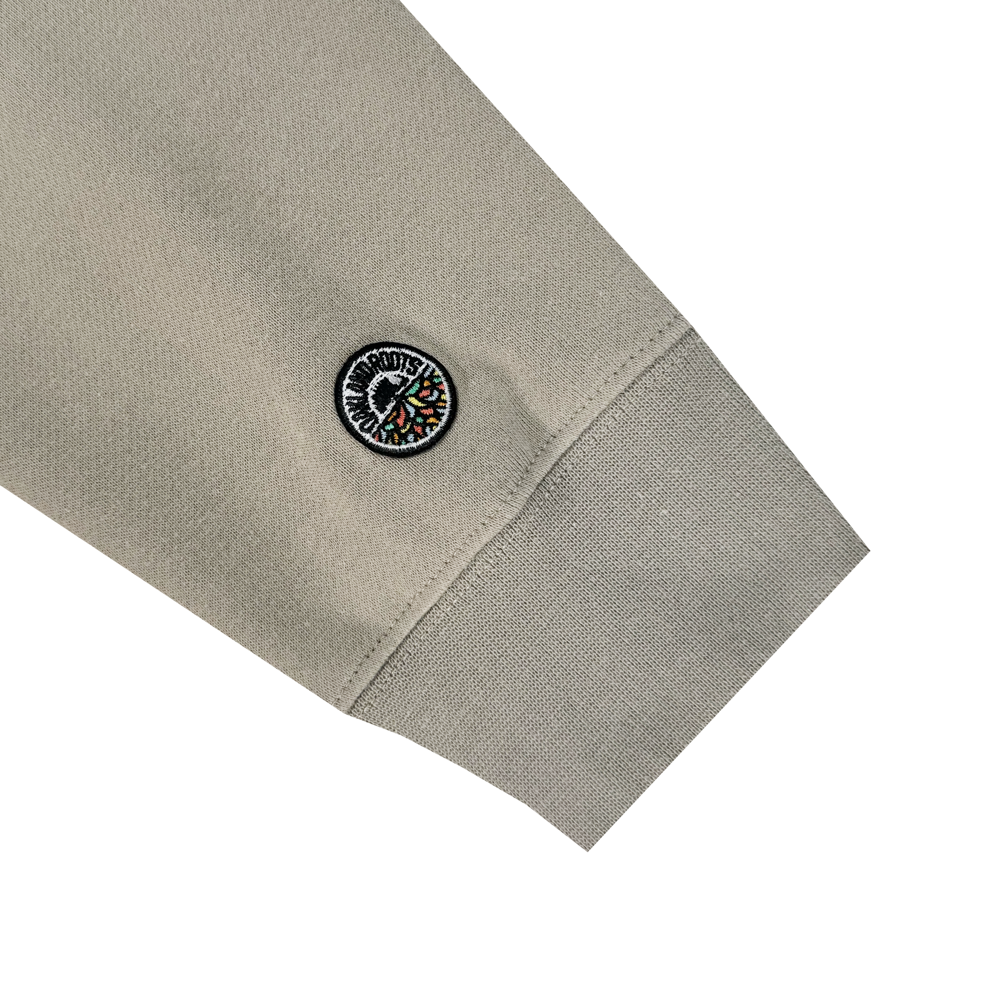 Close-up of a beige sleeve with a ribbed cuff from the Oakland Roots SC Classic Hoodie, showing a circular patch near the wrist. The patch features a colorful, abstract design with text inspired by Oakland Roots. The fabric looks smooth and slightly textured.