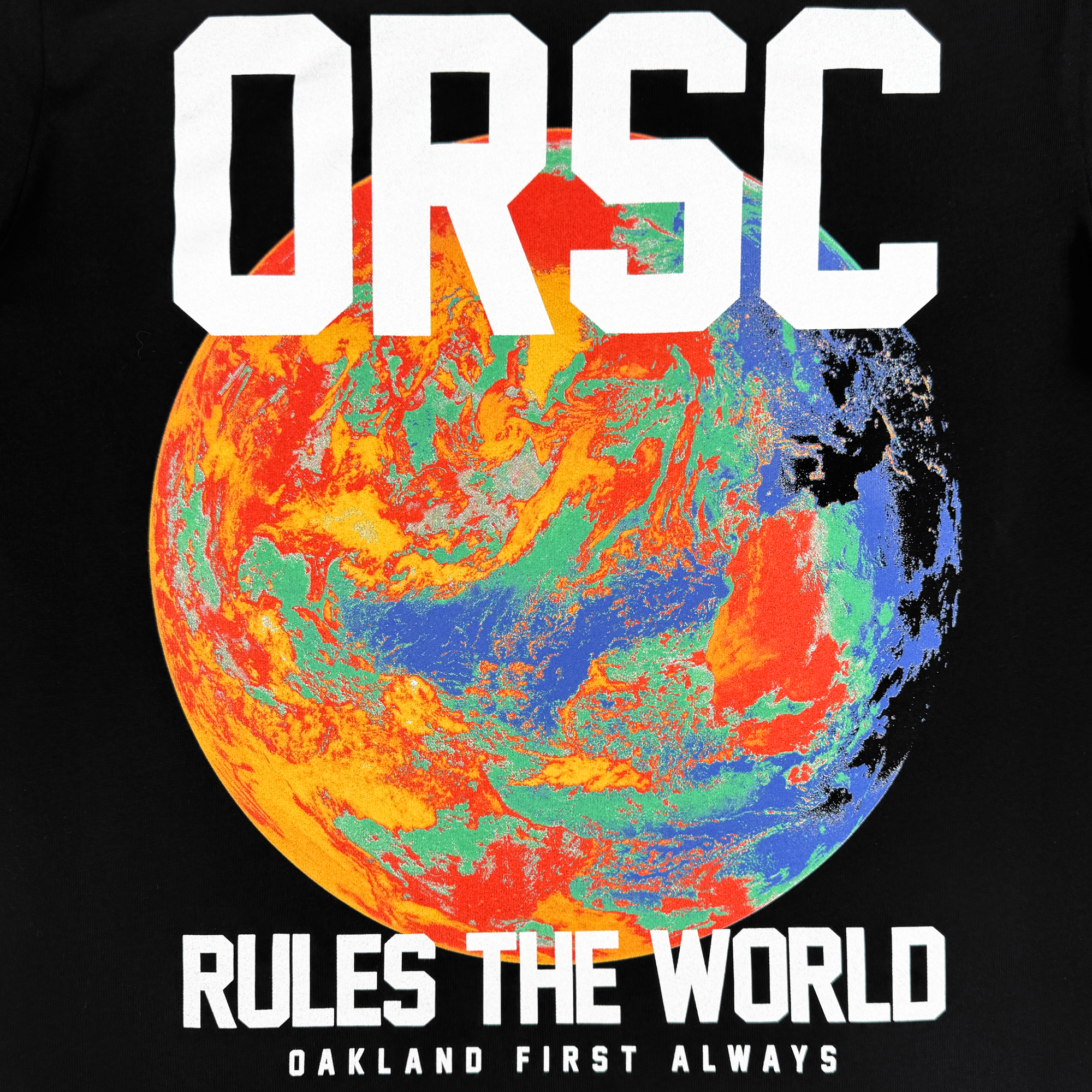 The OFA Worldwide Tee from Oakland Roots SC features a colorful, abstract Earth design with vibrant red, orange, blue, and green hues on a black background. Bold white text reads "ORSC" above and "RULES THE WORLD" below, with "Oakland First Always" at the bottom in smaller white text.