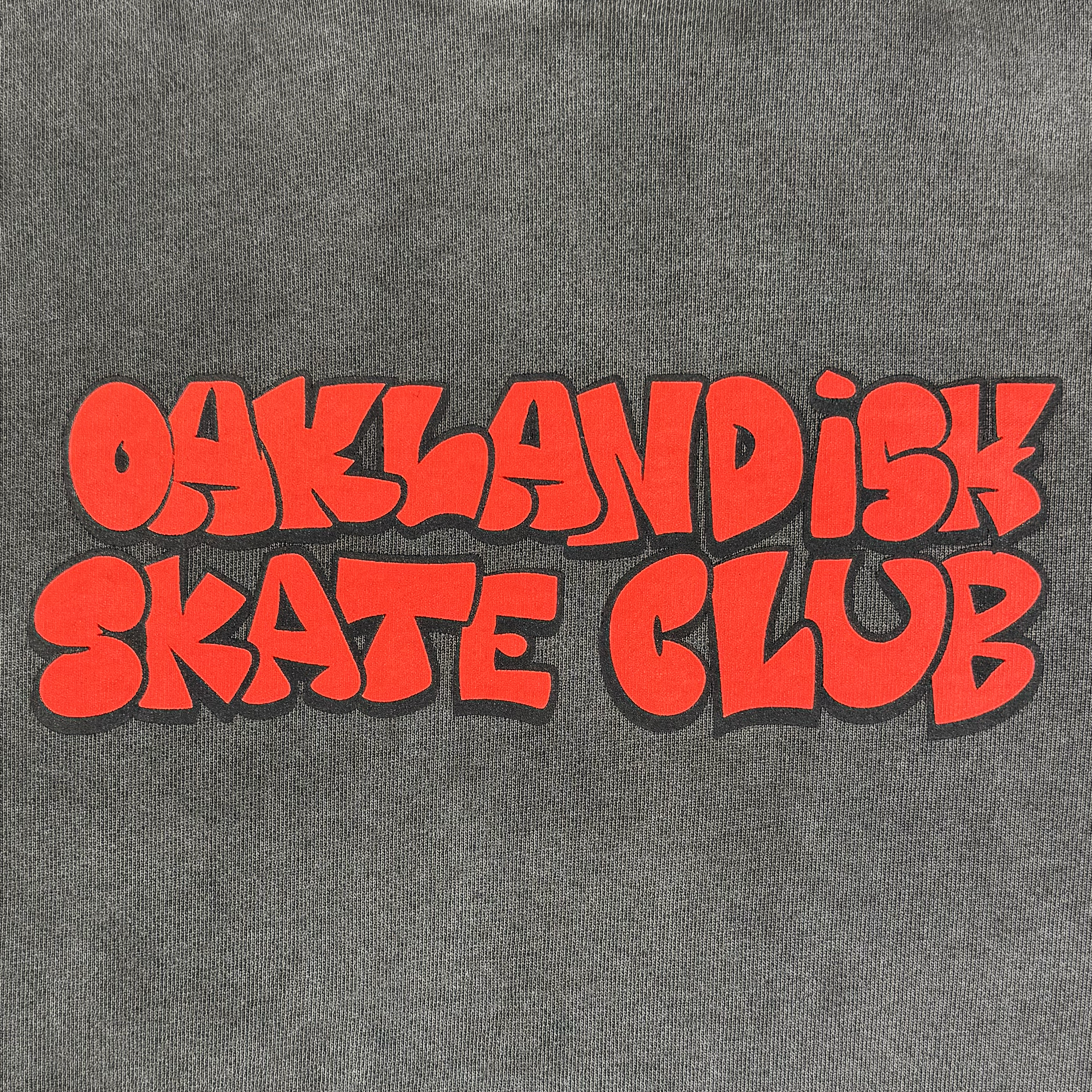 Bold, playful red text spells "Oaklandish Skate Club" in all caps with a black shadow on a gray Oaklandish hoodie. The rounded cartoon letters express the fun, energetic vibe of skateboard culture.