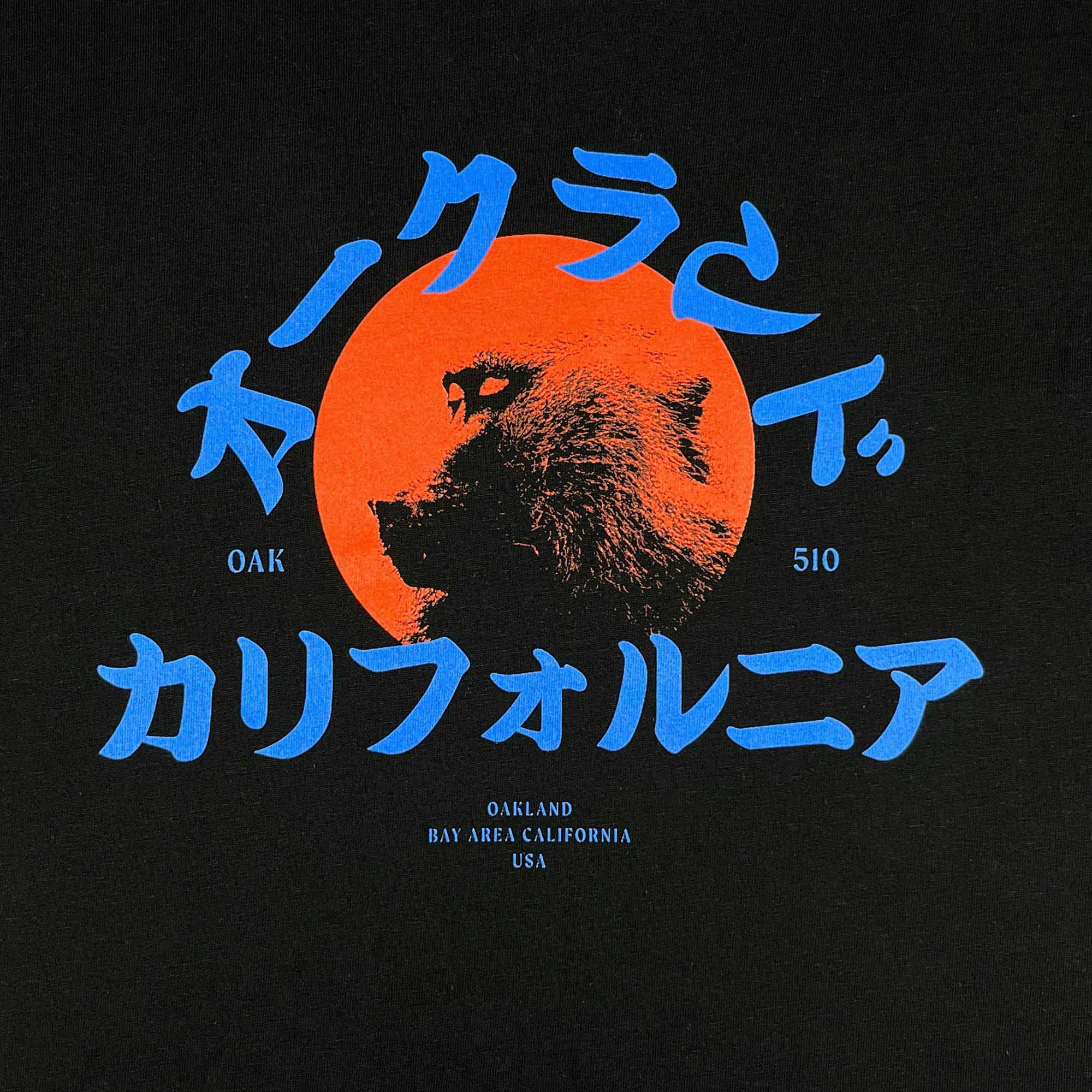 Close-up of red snow monkey graphic and blue Asian written characters, Oak 510 wordmark & Oakland Bay Area California wordmark on black t-shirt.