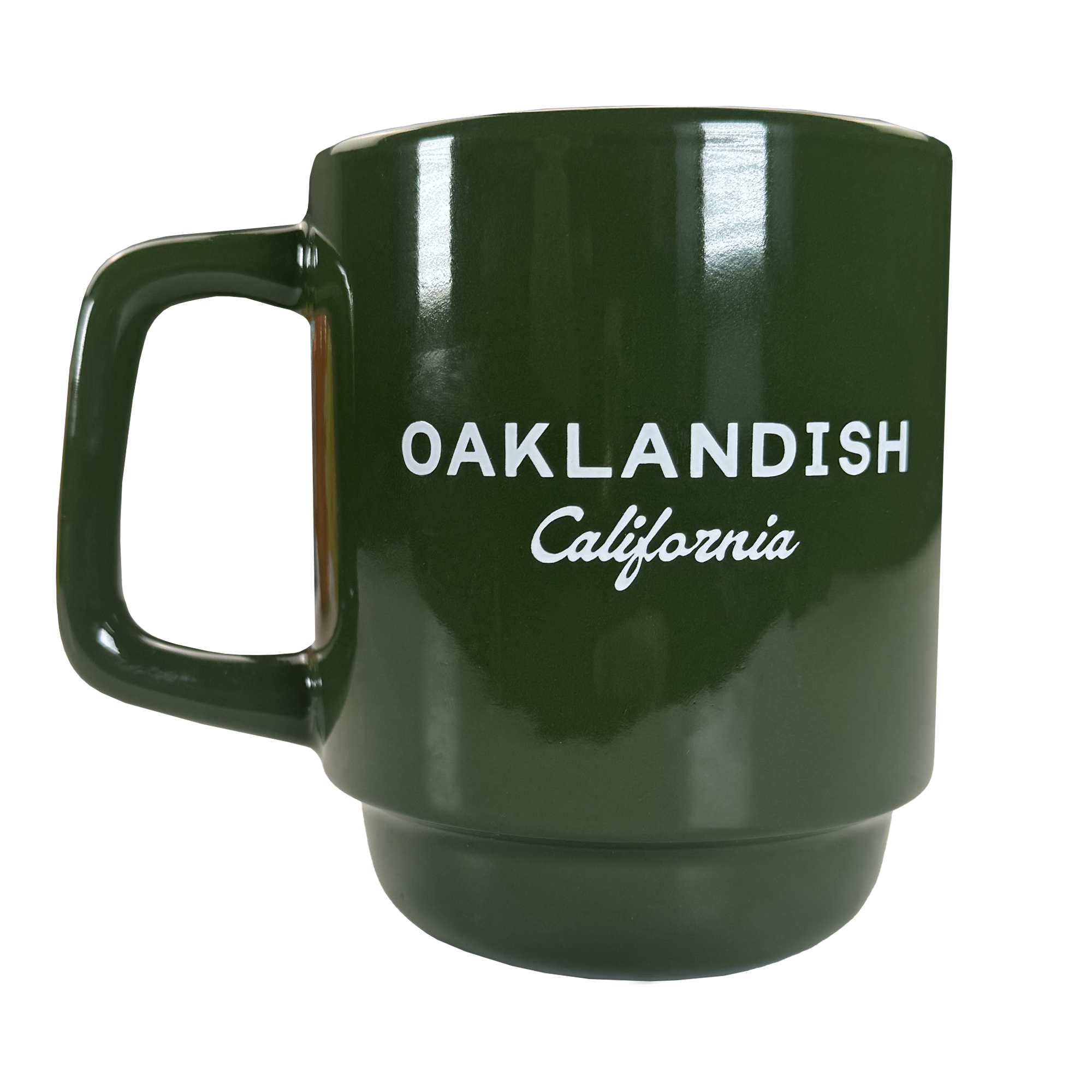 The Oaklandish Logo Stack Mug is a dark green ceramic mug with a large handle, featuring bold white "OAKLANDISH California" text on the front. Its modern design stands out against the plain background.