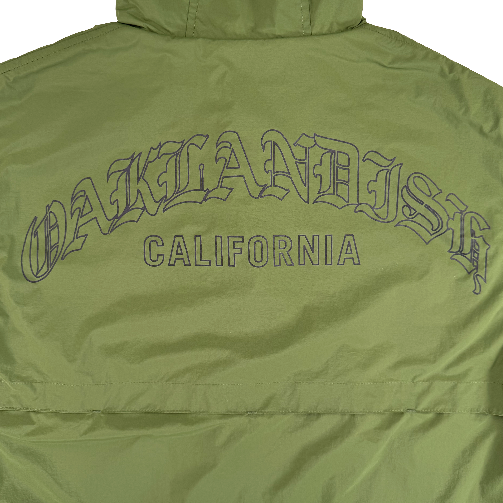 The Susurrus Track Top by Oaklandish is a light green nylon men's jacket with a hood, featuring bold “OAKLANDISH” lettering in black across the back and “CALIFORNIA” below. It sports classic fit, visible stitching, and a slight sheen for extra style.