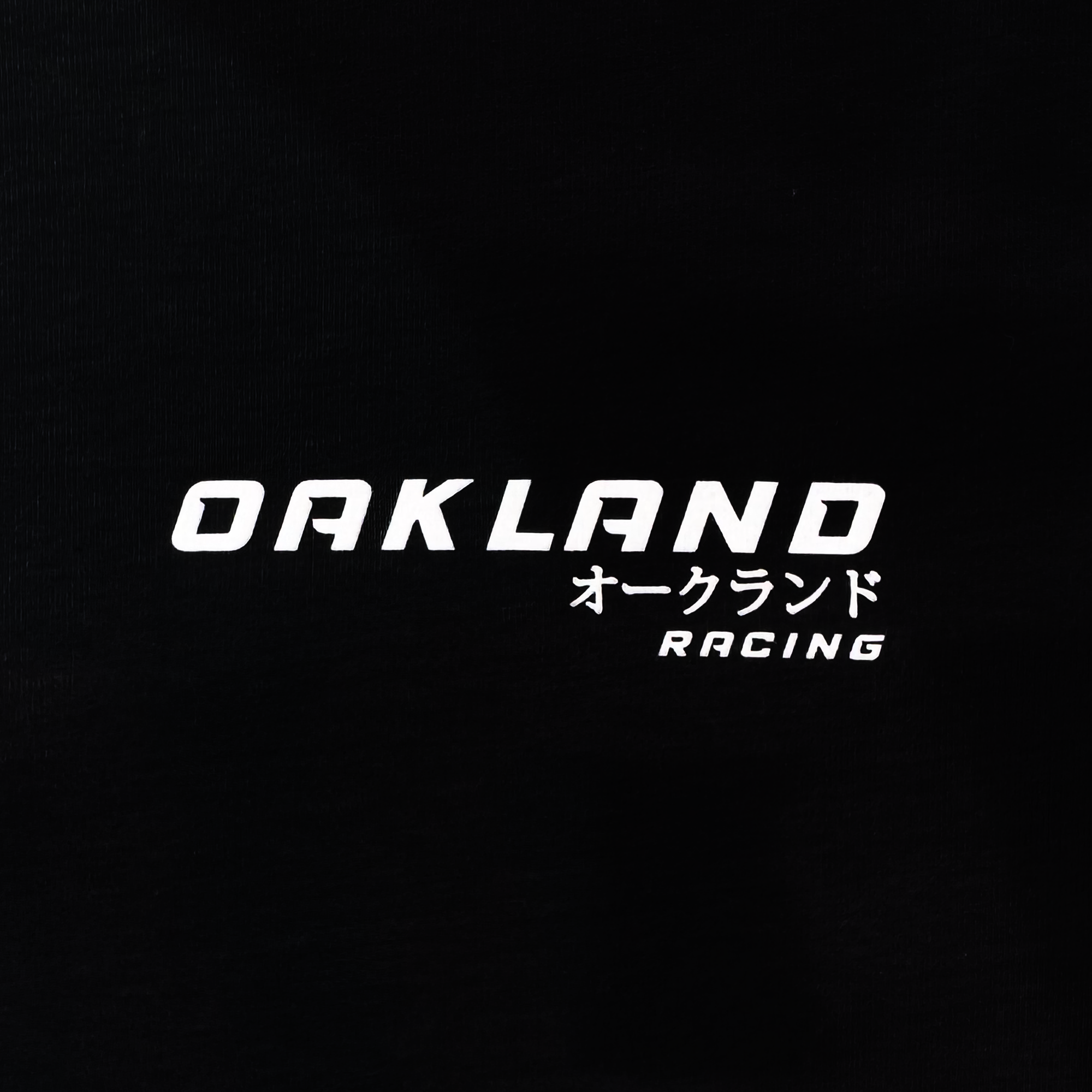 The Tuner Tee by Oaklandish is a classic fit men's 100% cotton t-shirt featuring "OAKLAND" in white text on a black background, with smaller Japanese characters and "RACING" stylishly shown underneath.