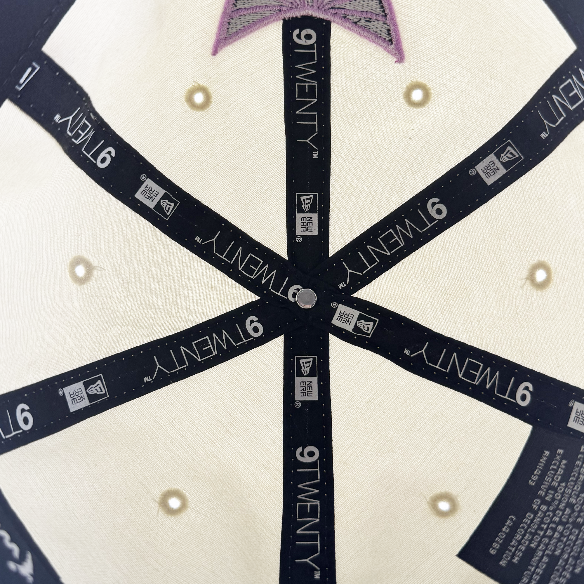 Close-up of the inside top of the cream GSV Logo 2 9TWENTY Hat by GSV. Features black inner seam covers with “9TWENTY” and “NEW ERA” logos, visible stitching, metal button at center, and purple Golden State Valkyries embroidery near the top.
