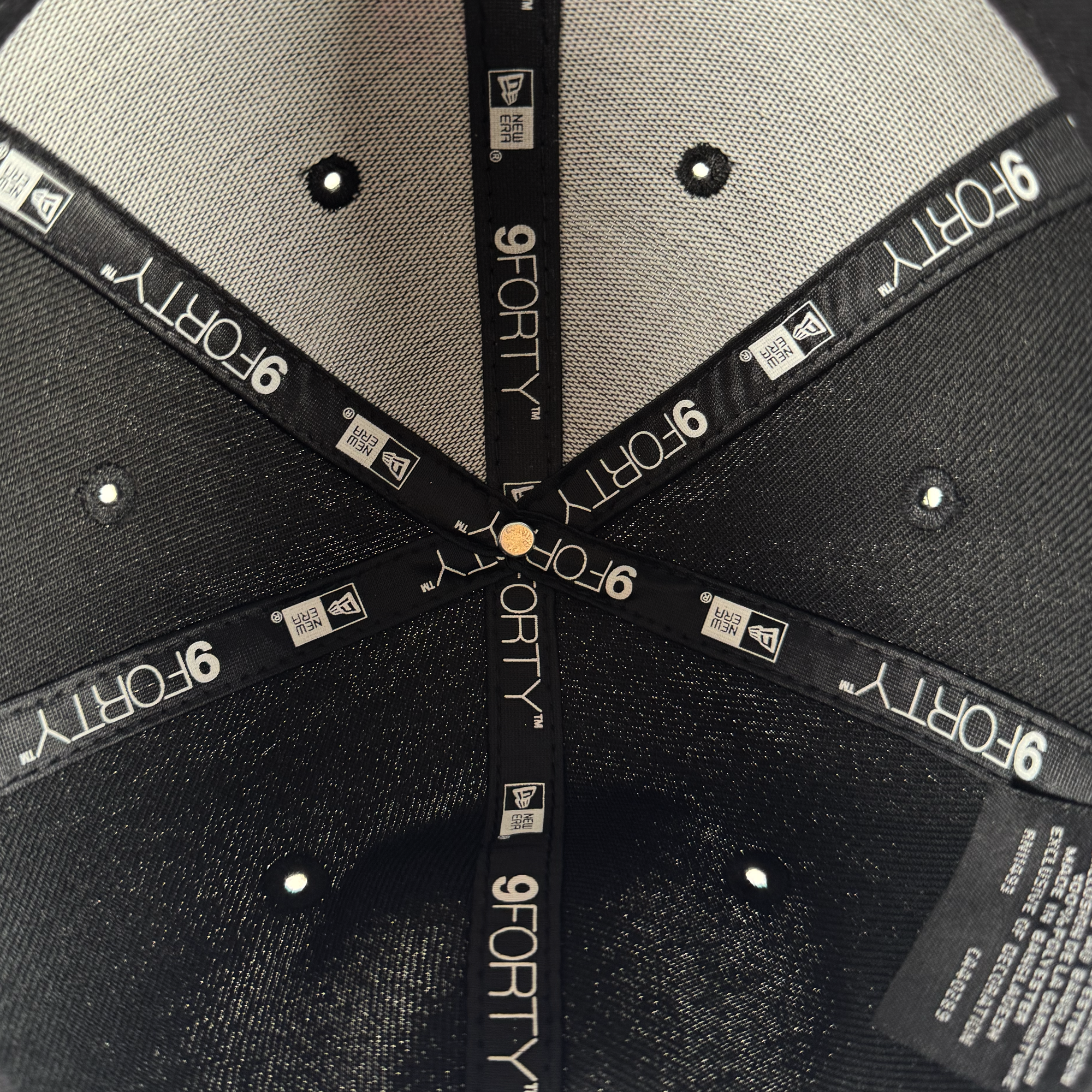 Close-up of the inside crown of a GSV Logo 9FORTY Snapback by GSV. Black fabric bands with "9FORTY" and the New Era logo intersect, secured by a gold button. The cap features light lining and visible ventilation holes.