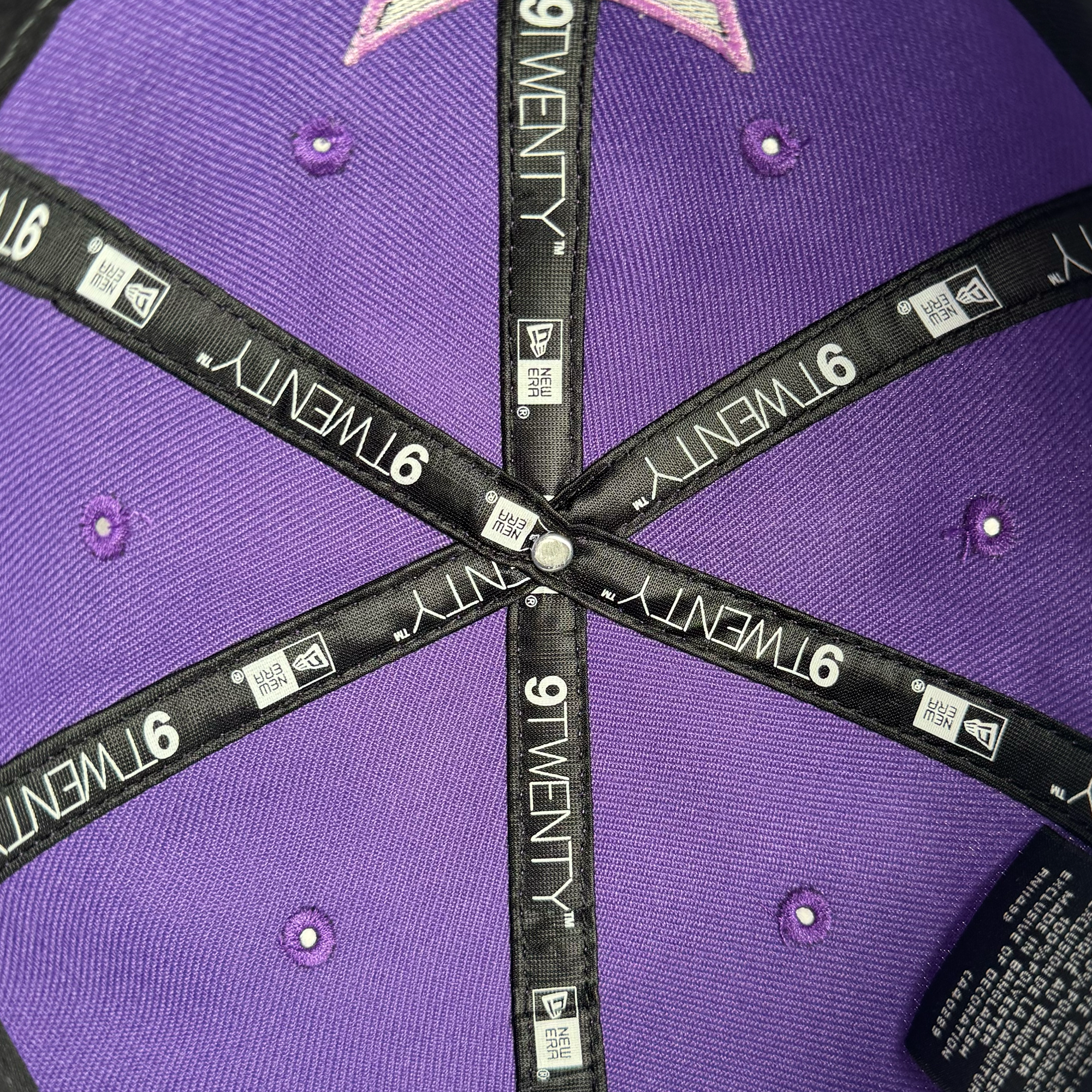 Close-up of the inside top of a purple GSV 9TWENTY Dad hat. Black fabric strips with white "9TWENTY" and "GSV" logos meet at the center with a metal rivet, showing purple fabric and stitched eyelets between the strips.