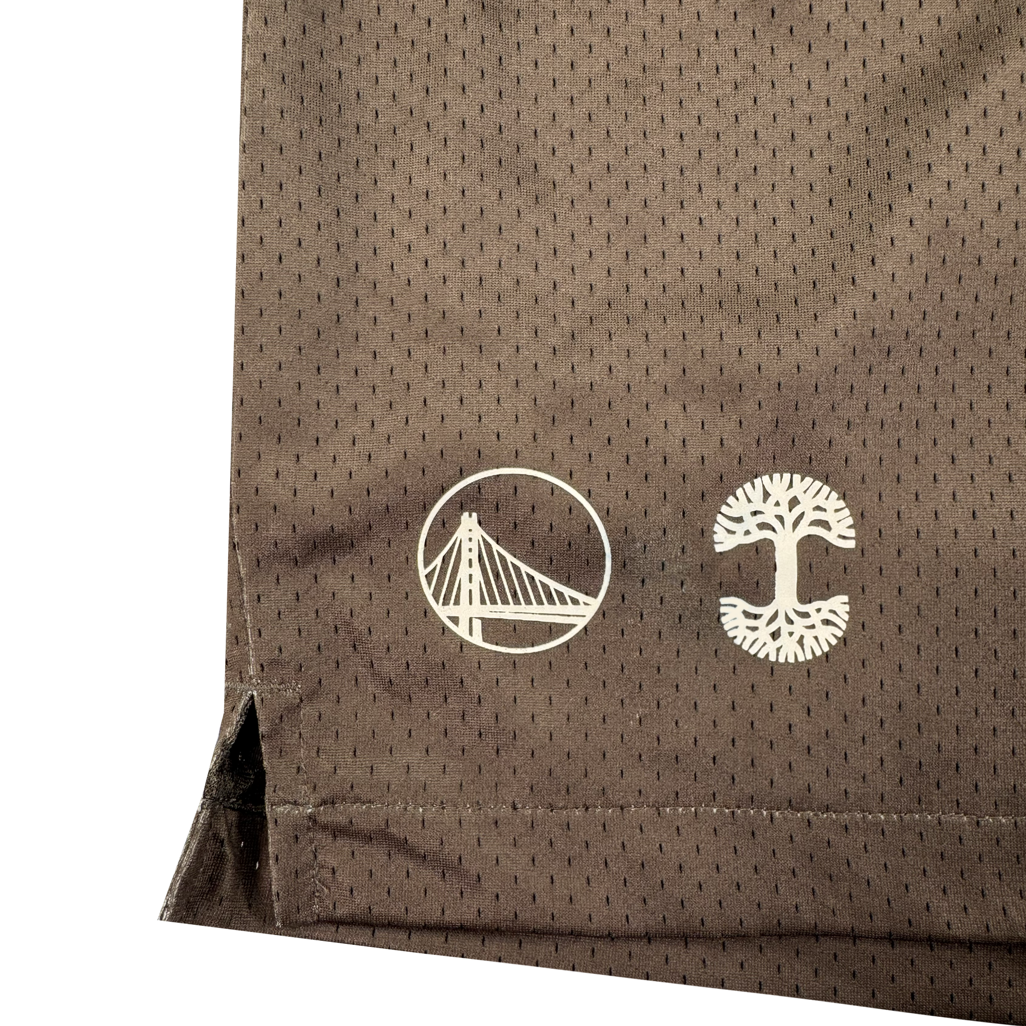 Close-up of brown perforated fabric from GSW's Arched Black-Letter Shorts, with two white logos—a suspension bridge and a stylized tree—plus a side slit at the hem. This unique piece is part of the Oaklandish collaboration.