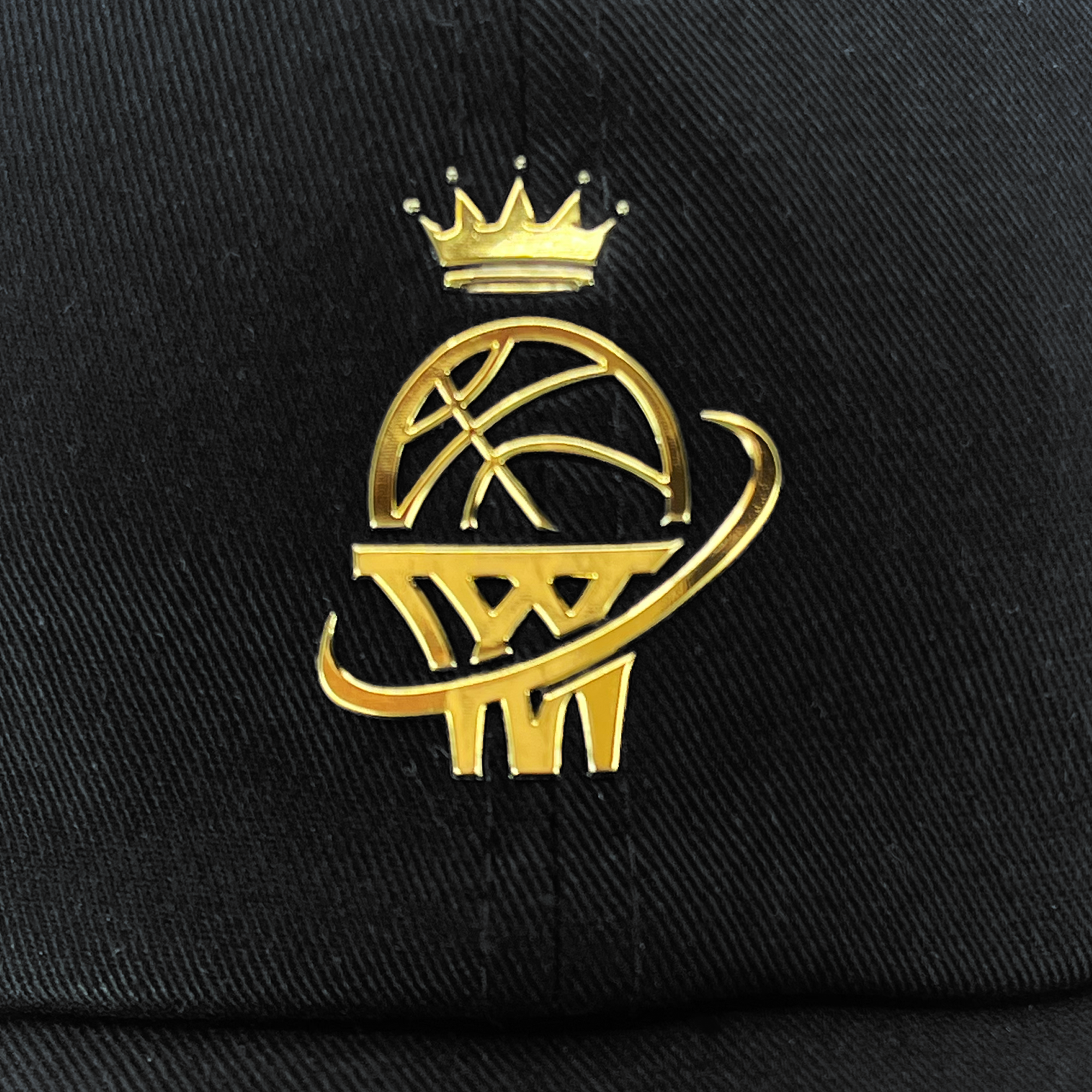 The WPBA Dad Hat by Oaklandish is a black hat that boasts an embroidered gold logo featuring a basketball with a crown above it and a stylistic swoosh resembling a ring around it, celebrating women's sports. The logo design also incorporates elements that mimic a basketball net at the bottom. This sleek design provides a luxurious look against the dark fabric.