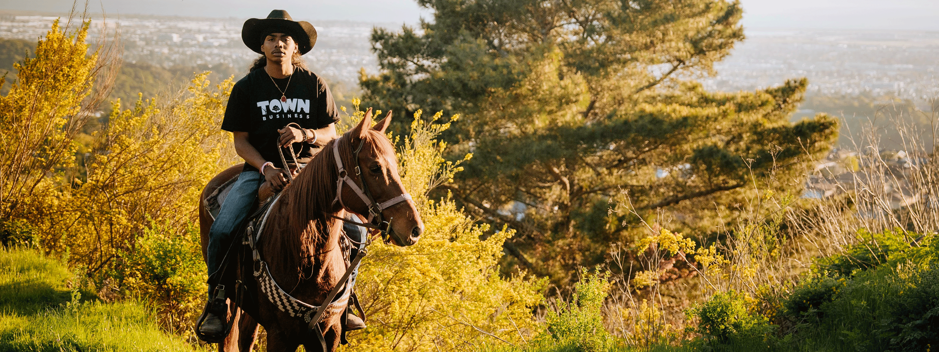 Man with a hat on horse on hill, with the city of Oakland in the background.