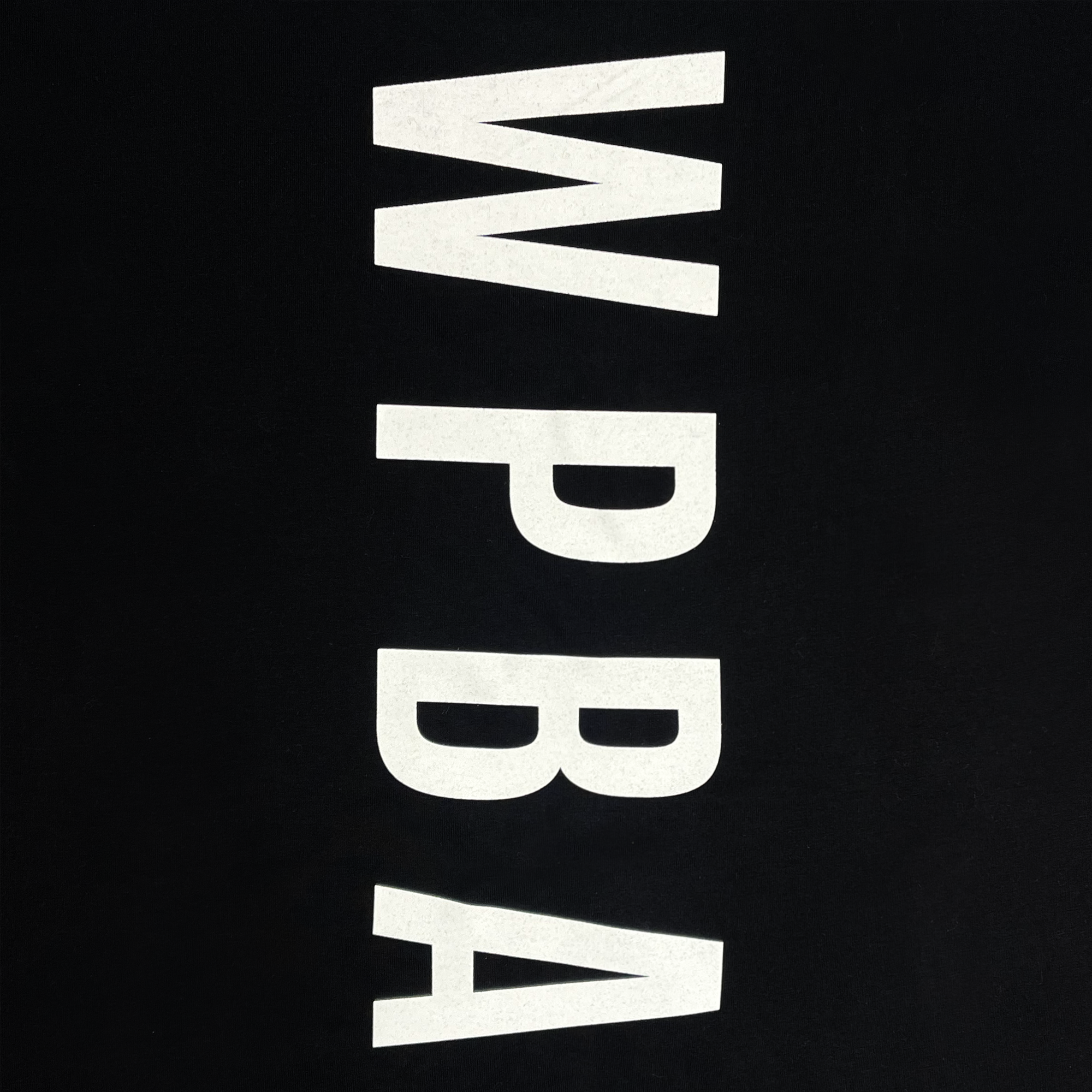 The WPBA Core LS Tee by Oaklandish features a black background with bold, white vertical letters "WPBA" arranged from top to bottom in the center of the design, symbolizing the empowerment of women's sports through the Women's Premier Basketball Association.