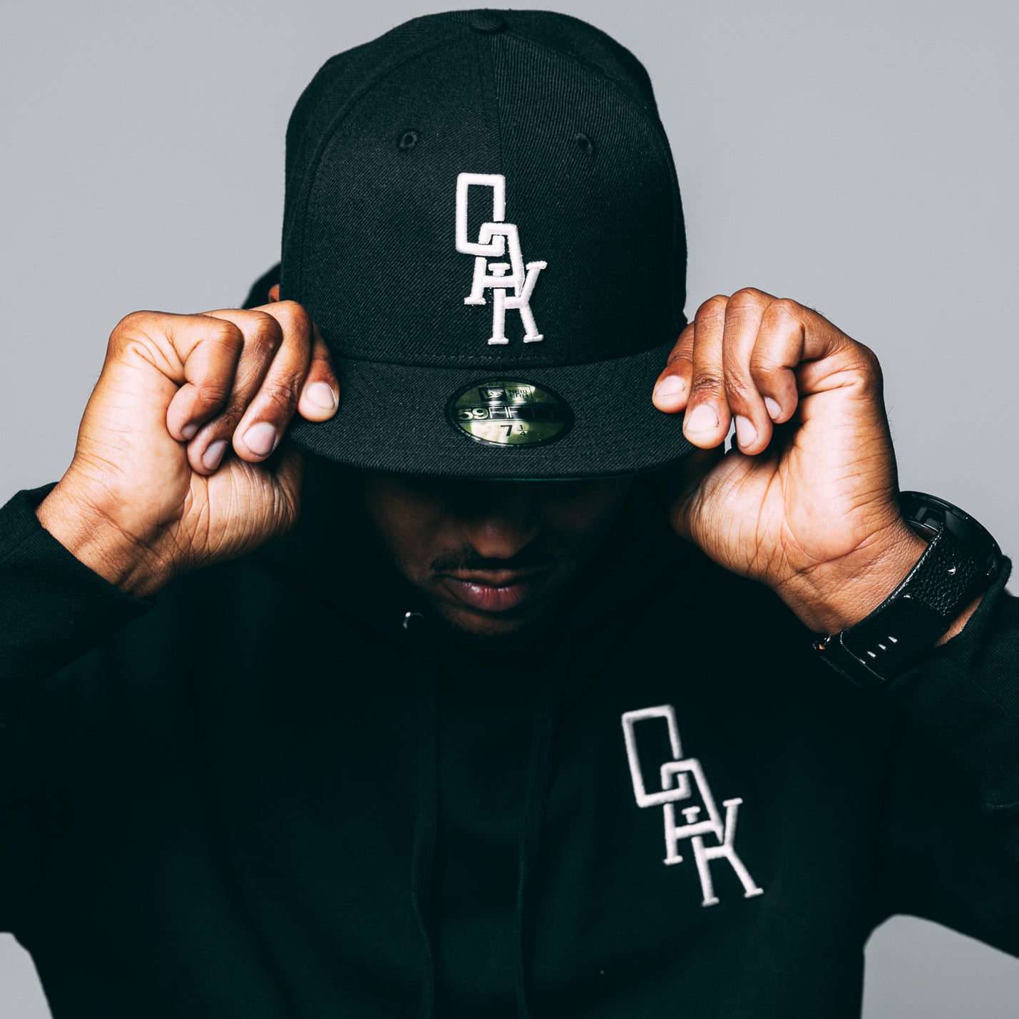 Man wearing a black New Era cap with white embroidered OAK wordmark on the crown.