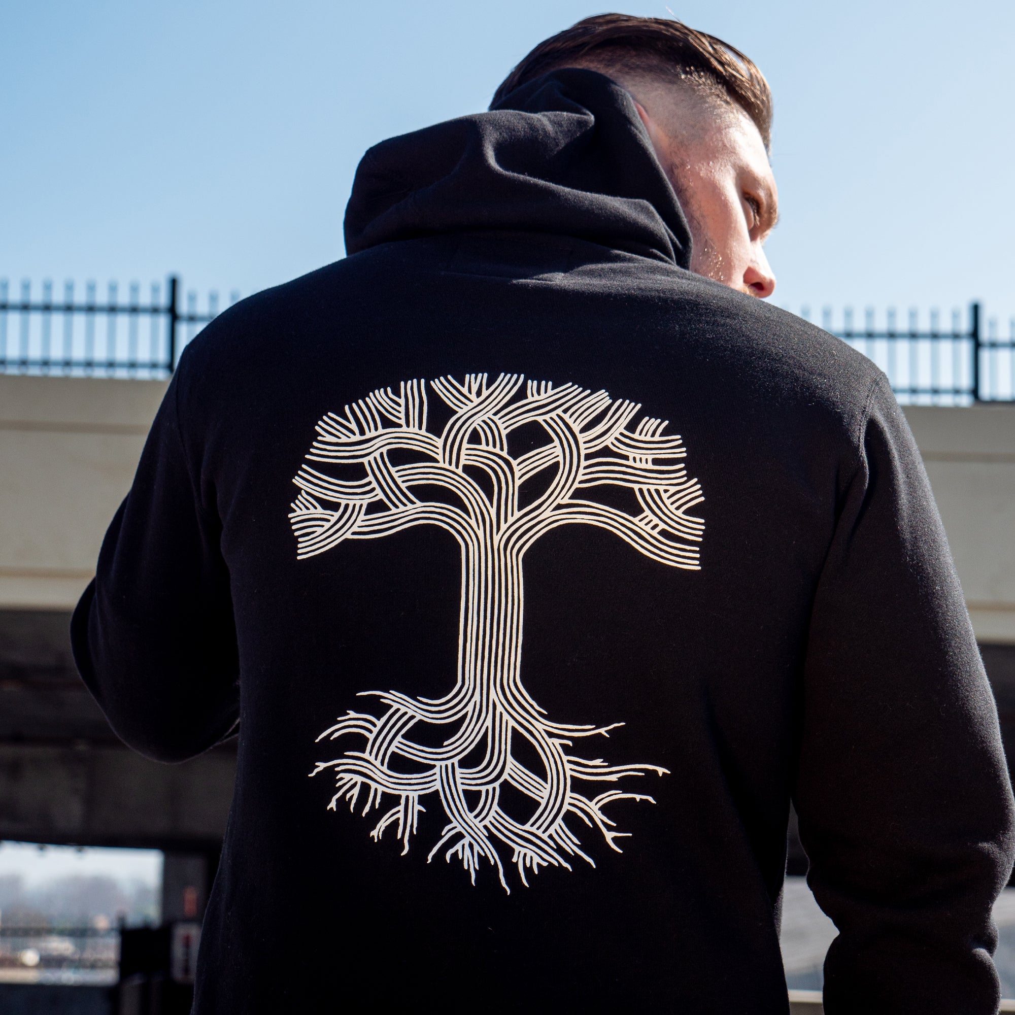 Detailed close up of front chest of Male model wearing black hoodie with Oaklandish tree logo on back.