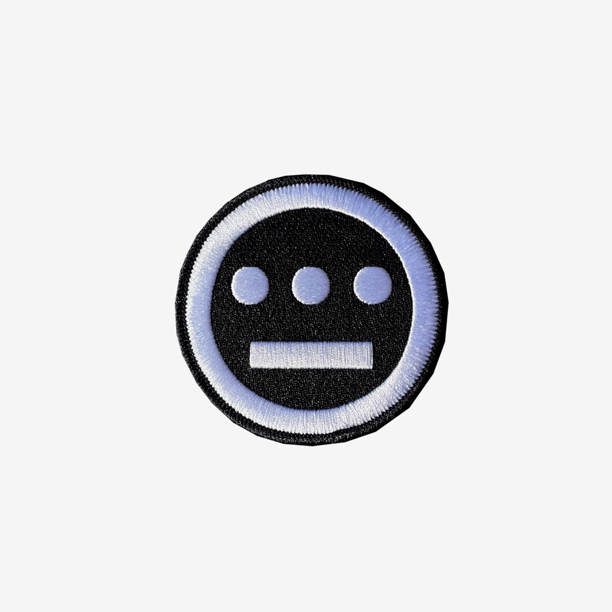 The Hiero Logo Patch by Hieroglyphics is a circular iron-on patch featuring intricate embroidery on a black background with a white embroidered border. The detailed interior design showcases three horizontally arranged white dots above a white horizontal line, resembling eyes and a mouth. It's the ideal accessory for adding unique flair to your collection.