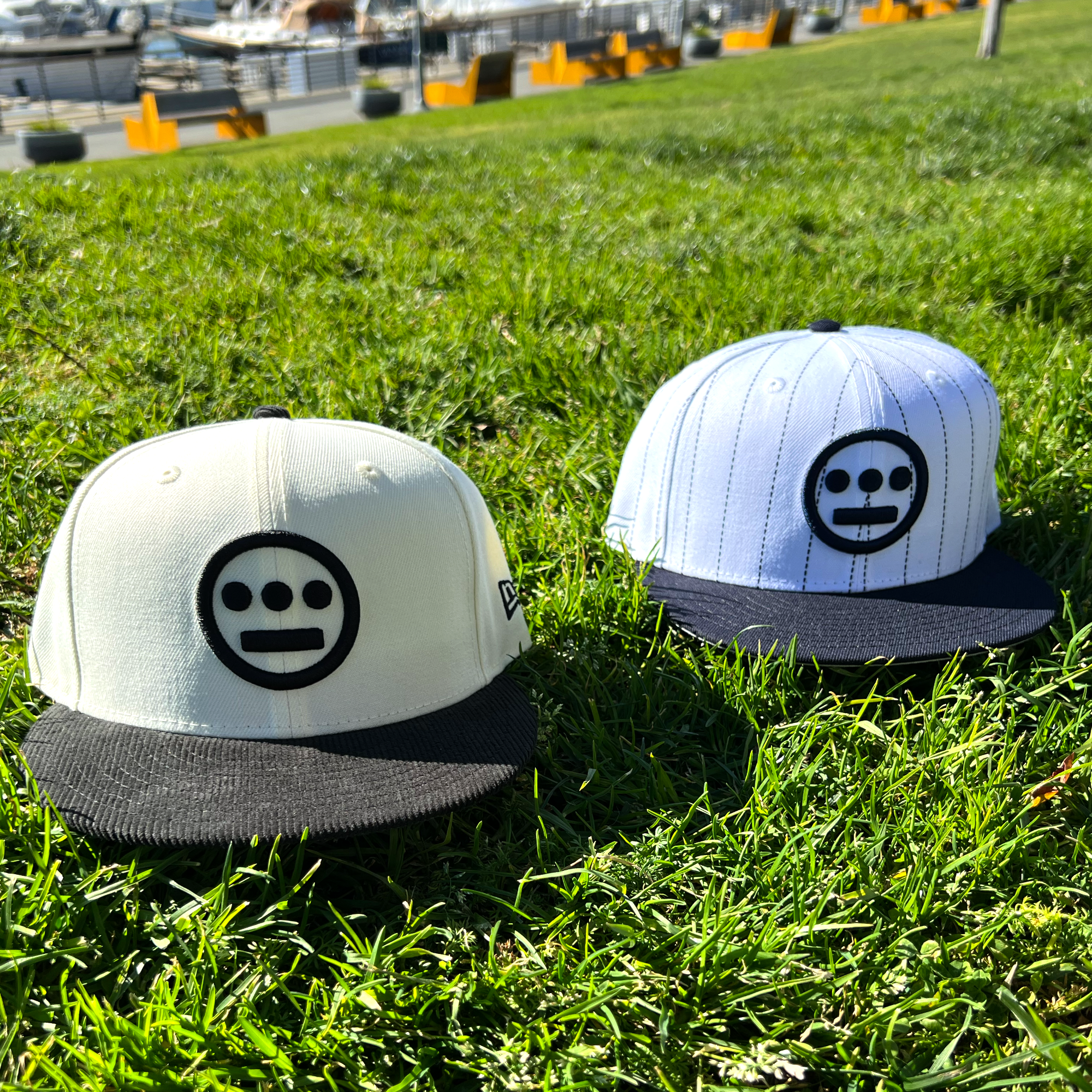 Tow different New Era 59FIFTY Hieroglyphics fitted hats outdoors on grass.