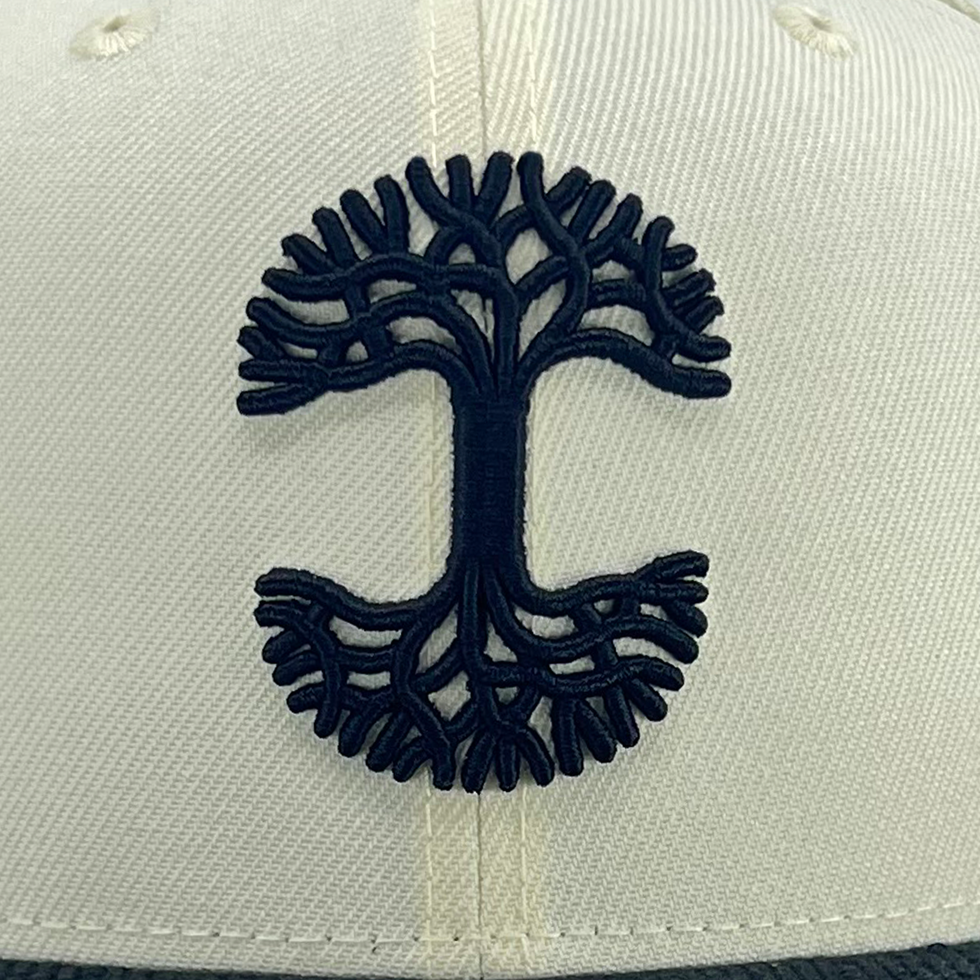 The New Era X Oaklandish Classic Cord 59FIFTY Fitted Cap by Oaklandish features a black embroidered tree design. The elaborate branches and roots extend symmetrically from the trunk in a circular pattern, resembling a detailed graphic icon on the white cap. Made from textured fabric, this hat exudes an unmistakable Oaklandish vibe.