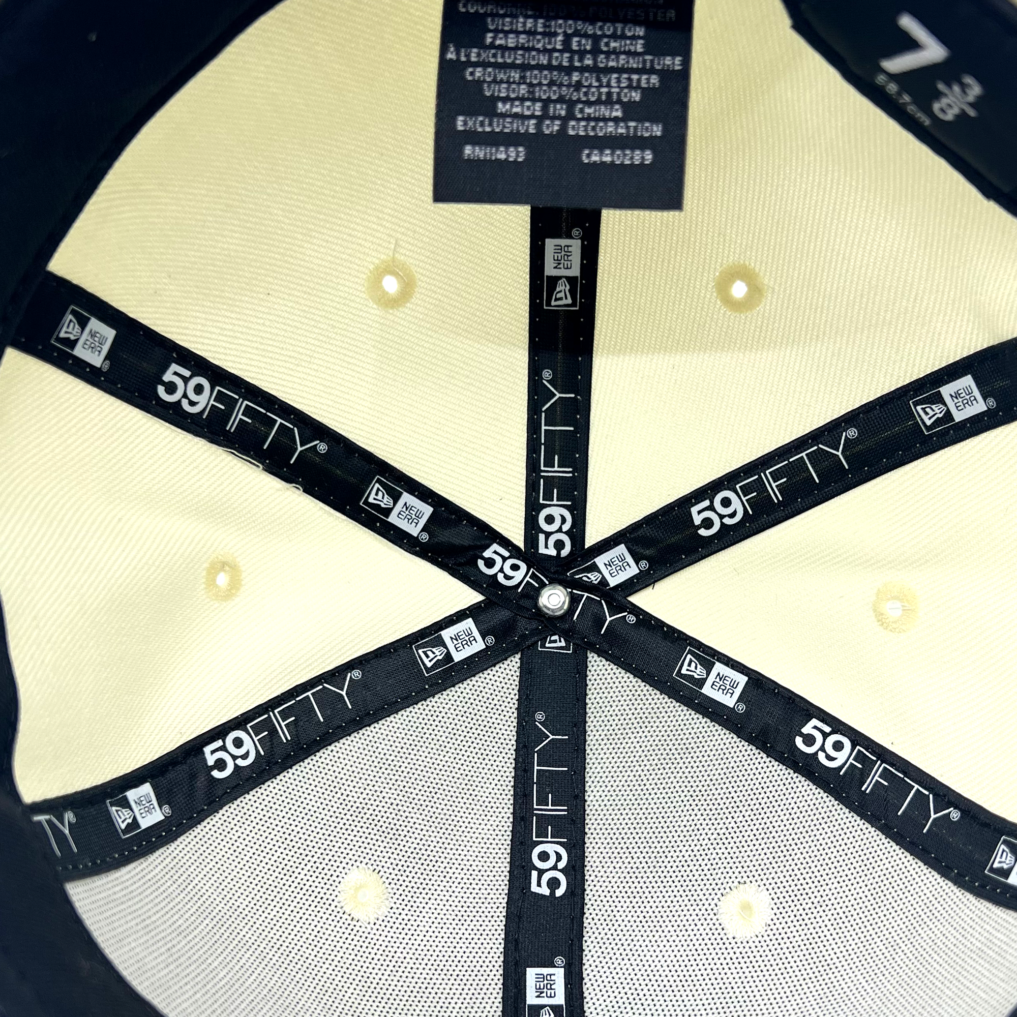 The underside view of the black New Era X Oaklandish Classic Cord 59FIFTY Fitted Cap reveals its internal structure with black bands marked "59FIFTY" and "New Era." A label at the top indicates it is made in China, showing care instructions and material composition. The cap size is noted as 7 1/8, with beige and grey interior fabric.