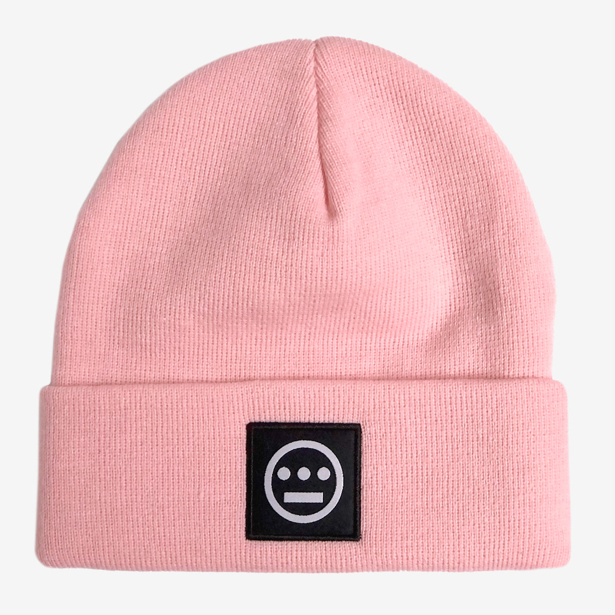 The Hiero Logo Cuff Beanie by Hieroglyphics is a light pink beanie featuring a folded edge and a black rectangular patch on the front. The patch showcases a white minimalist face design, reminiscent of ancient hieroglyphics, with a horizontal line for a mouth and three small circles above it, resembling eyes and a nose.