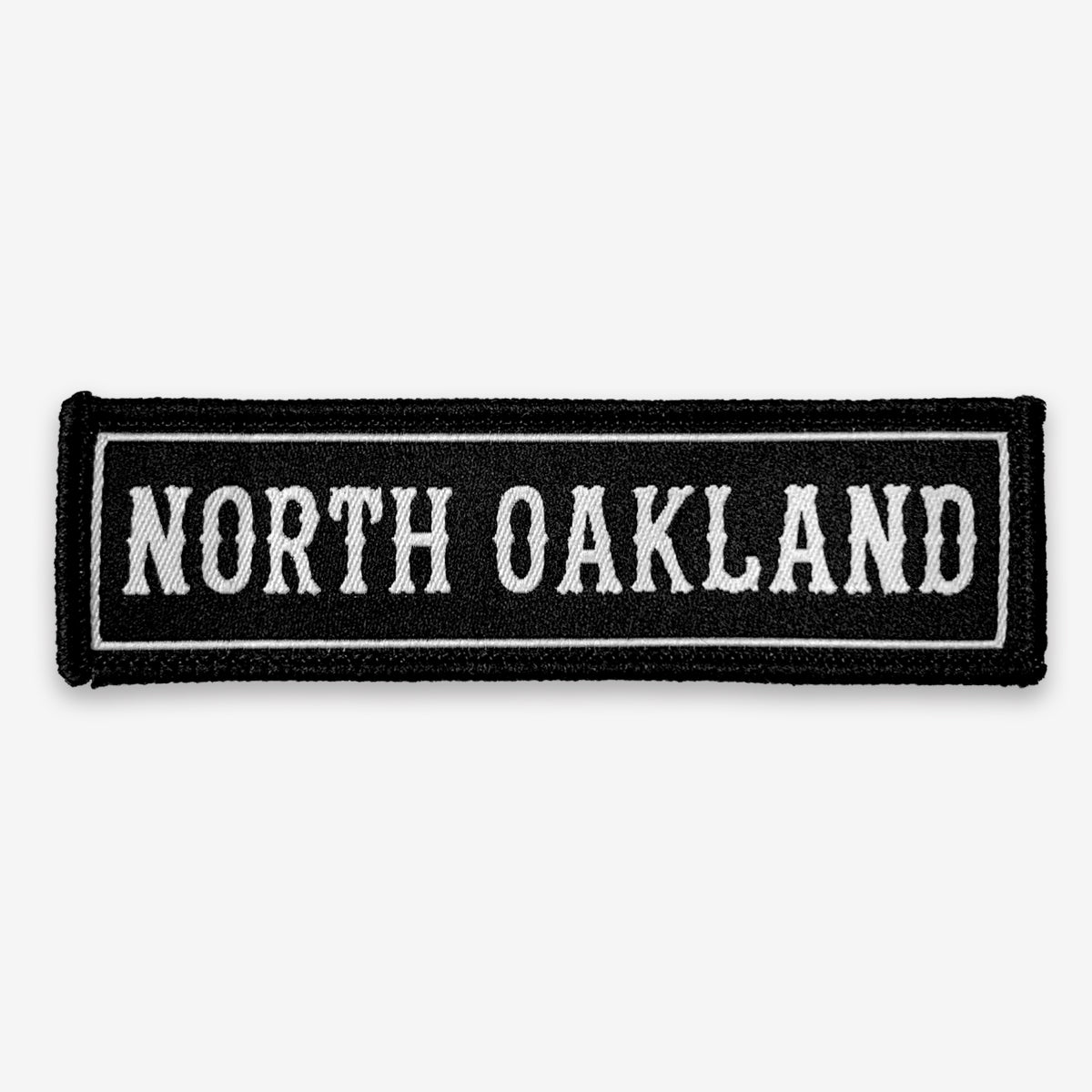 Black rectangle fabric iron patch, outlined with white line and capitalized word mark “NORTH OAKLAND.”