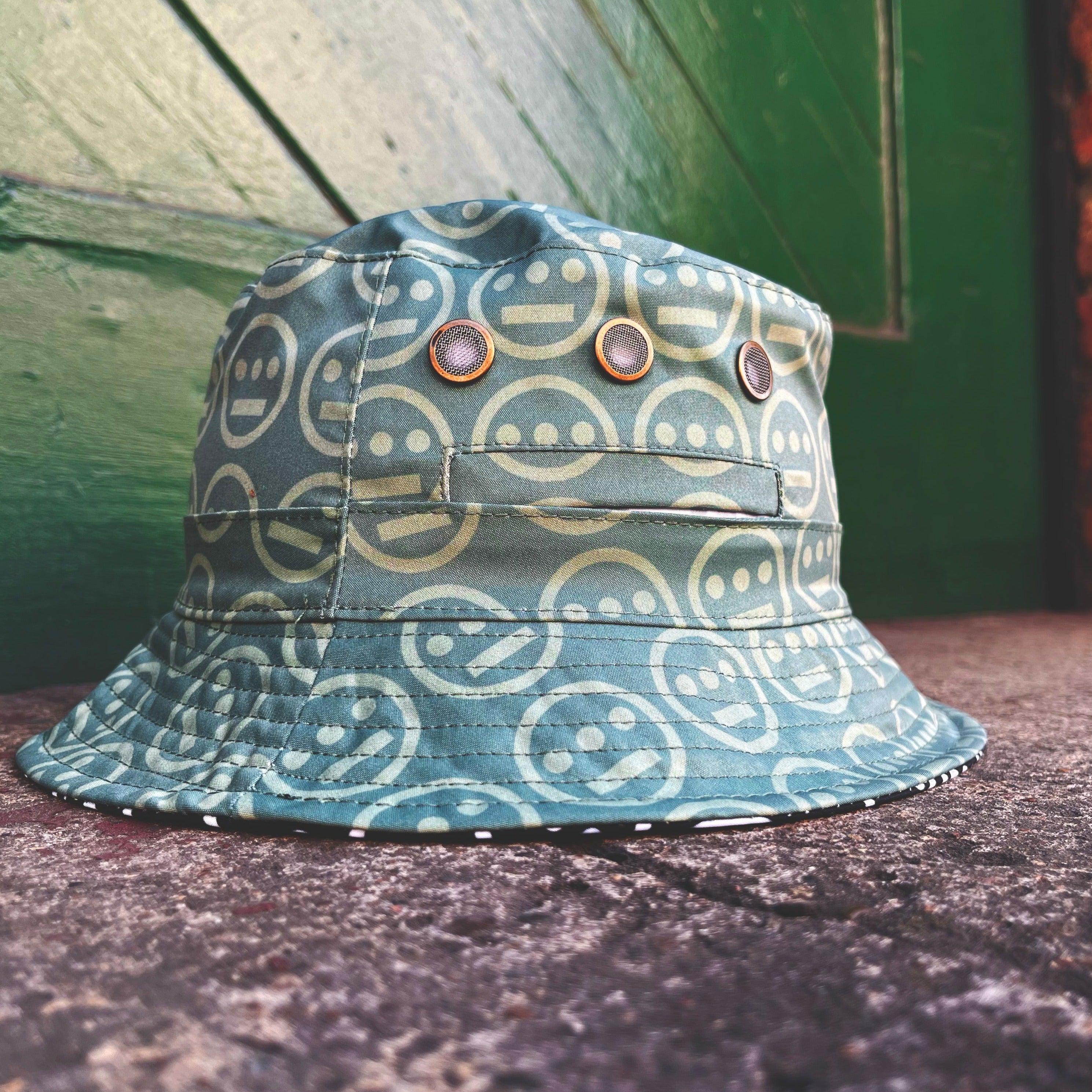 The green side of a reversible bucket hat with light green Hieroglyphics hip-hop logo on repeat sitting outdoors.