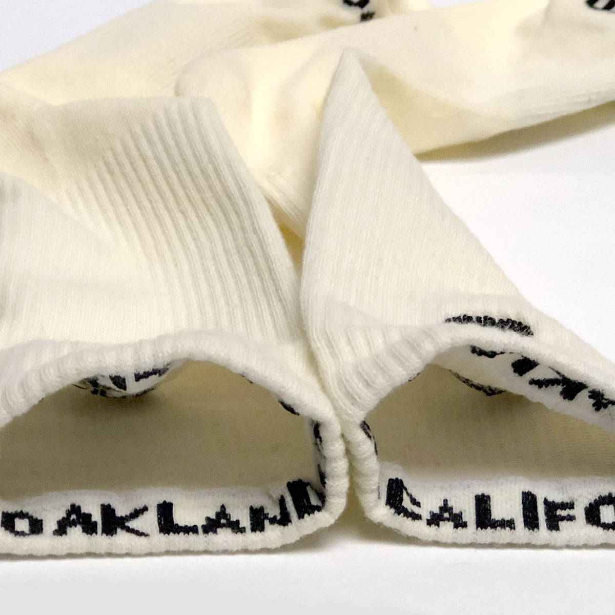 Close-up of the top of cream & black crew socks insides to expose the Oaklandish & California wordmarks - one on each of the rims. 