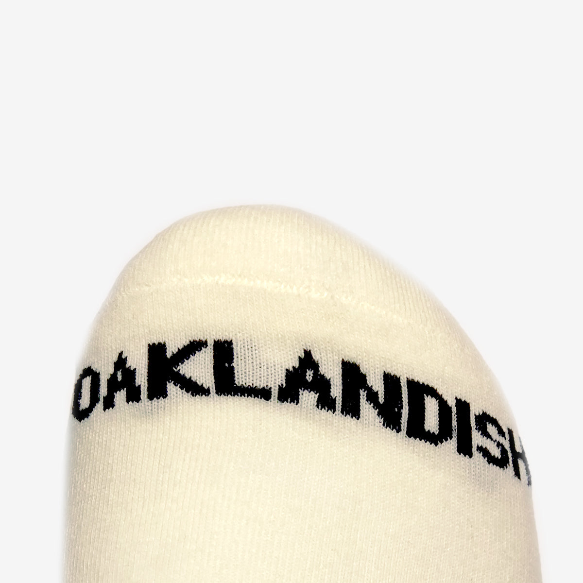 Close up of a black Oaklandish wordmark on the toe of cream crew socks.