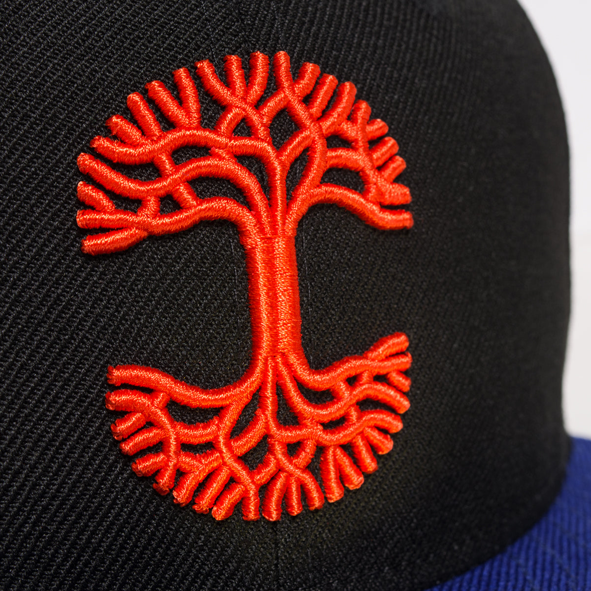 Close-up of red embroidered Oaklandish tree logo on the crown of a black New Era cap.