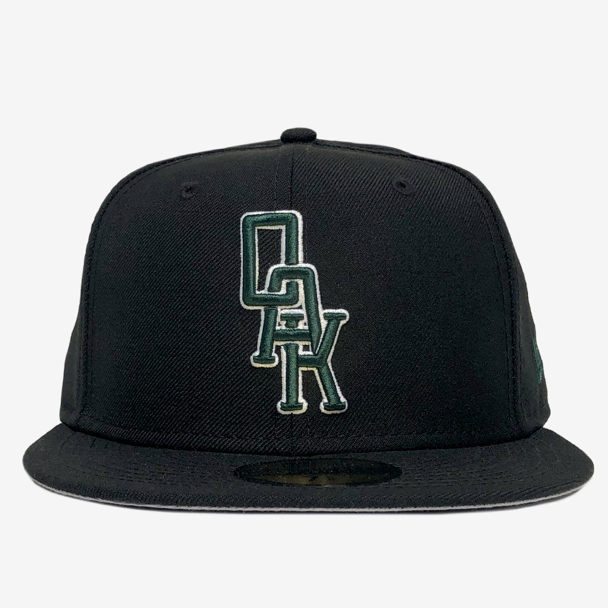 An Oaklandish New Era OAK 59FIFTY Fitted Cap in black, featuring an embroidered OAK logo in green and white on the front. The structured crown has a small green New Era cap logo on the side. The background is a plain, light grey.