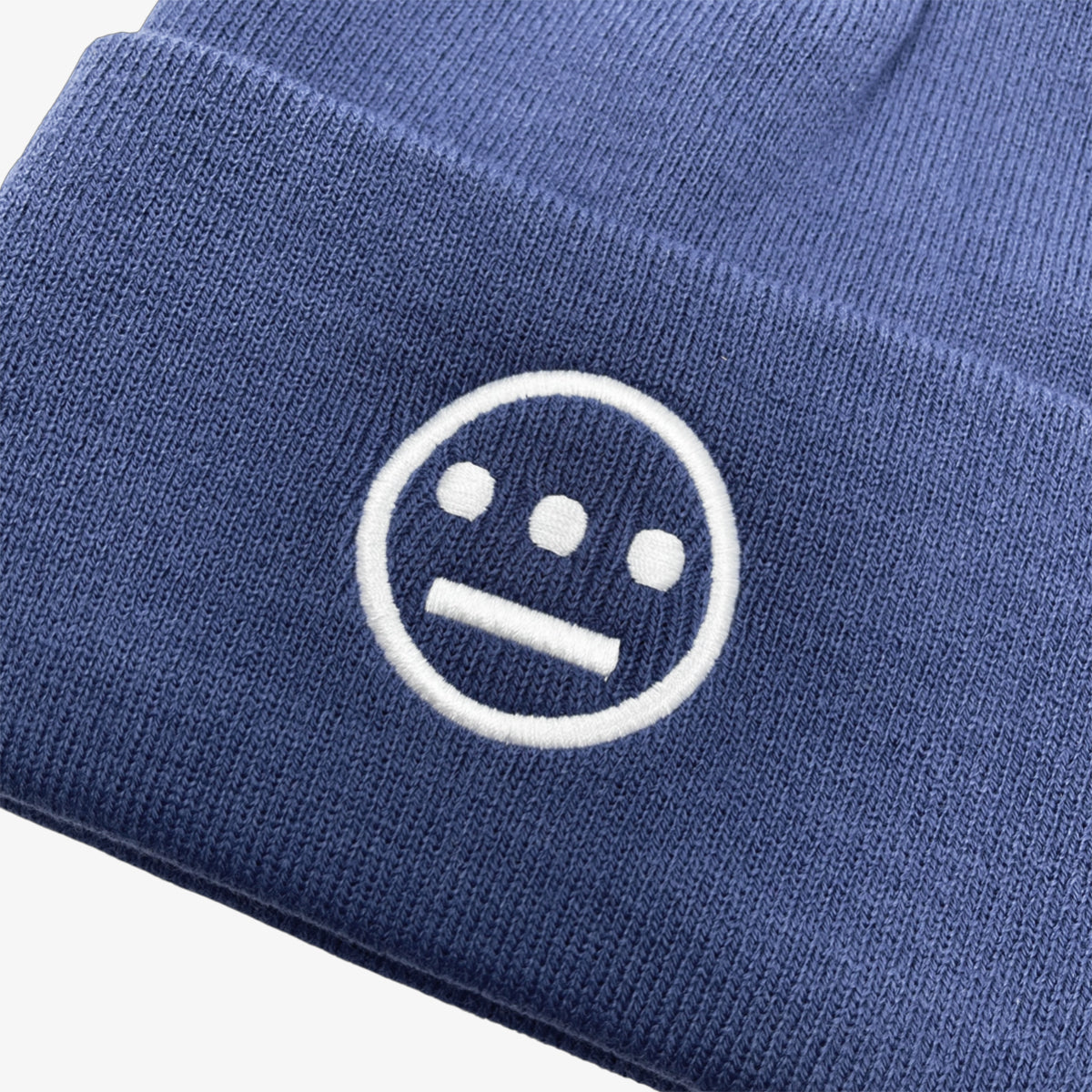 Close-up of white embroidered Hieroglyphics hip hop logo on front cuff of a navy cuffed beanie.