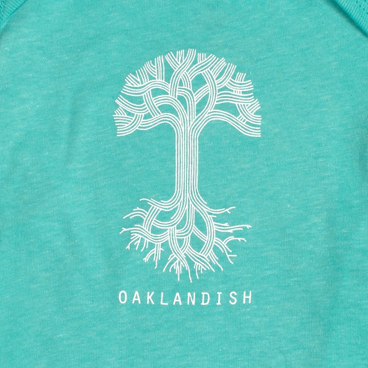 An infant size one-piece by Oaklandish, crafted from 100% cotton in teal, features a white graphic of a stylized tree with intricate branching roots at the top and bottom. Beneath the tree, "OAKLANDISH" is printed in capital white letters, ideal for little ones who want to express hometown pride.